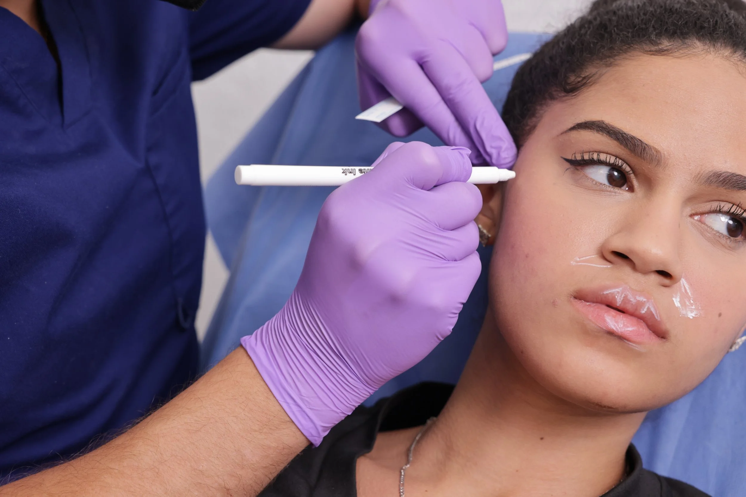 A person with makeup is receiving a cosmetic injection or treatment from a healthcare professional wearing purple gloves.