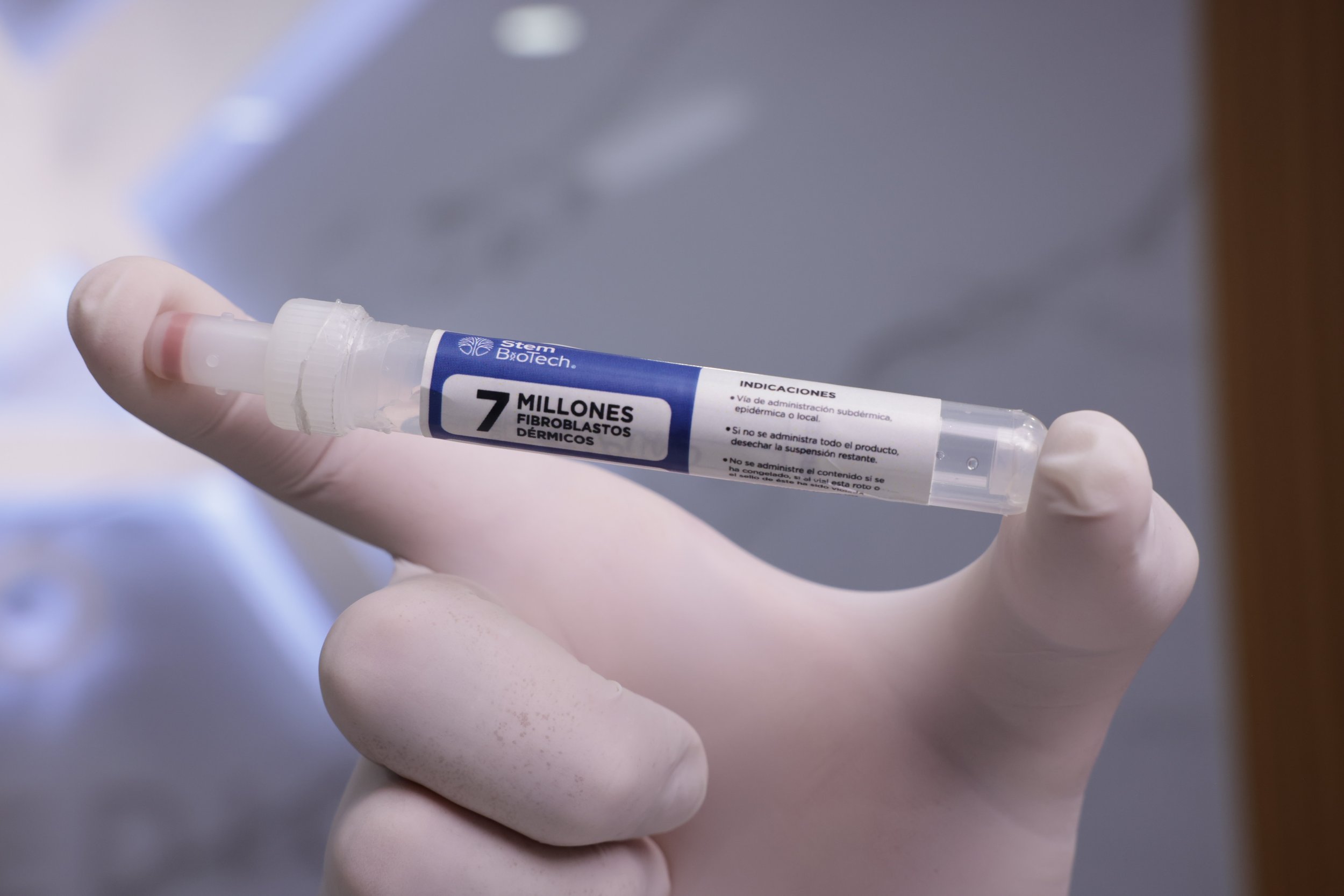 A person wearing white gloves holding a syringe with a label indicating '7 million fibroblast dermal' and some instructions in Spanish.