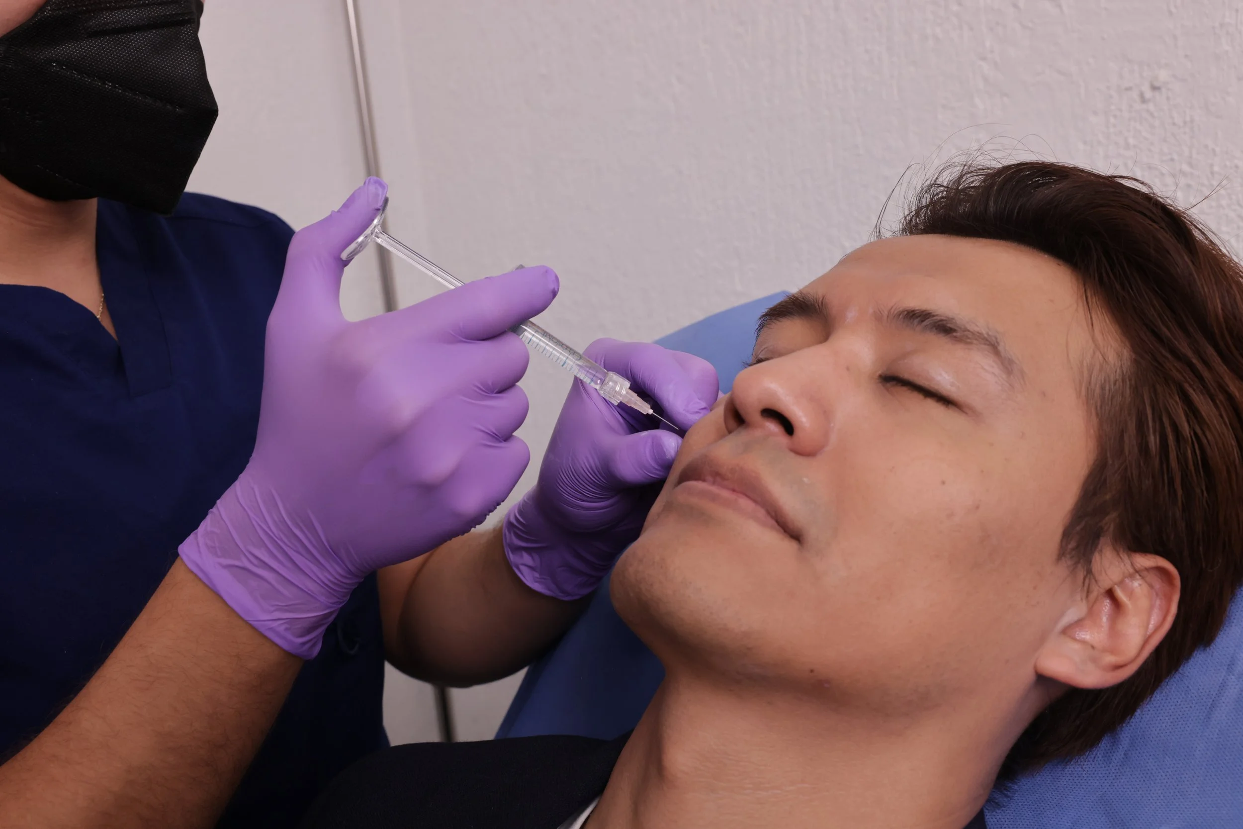 A person receiving a cosmetic injection or treatment from a healthcare professional wearing purple gloves in a clinical setting.
