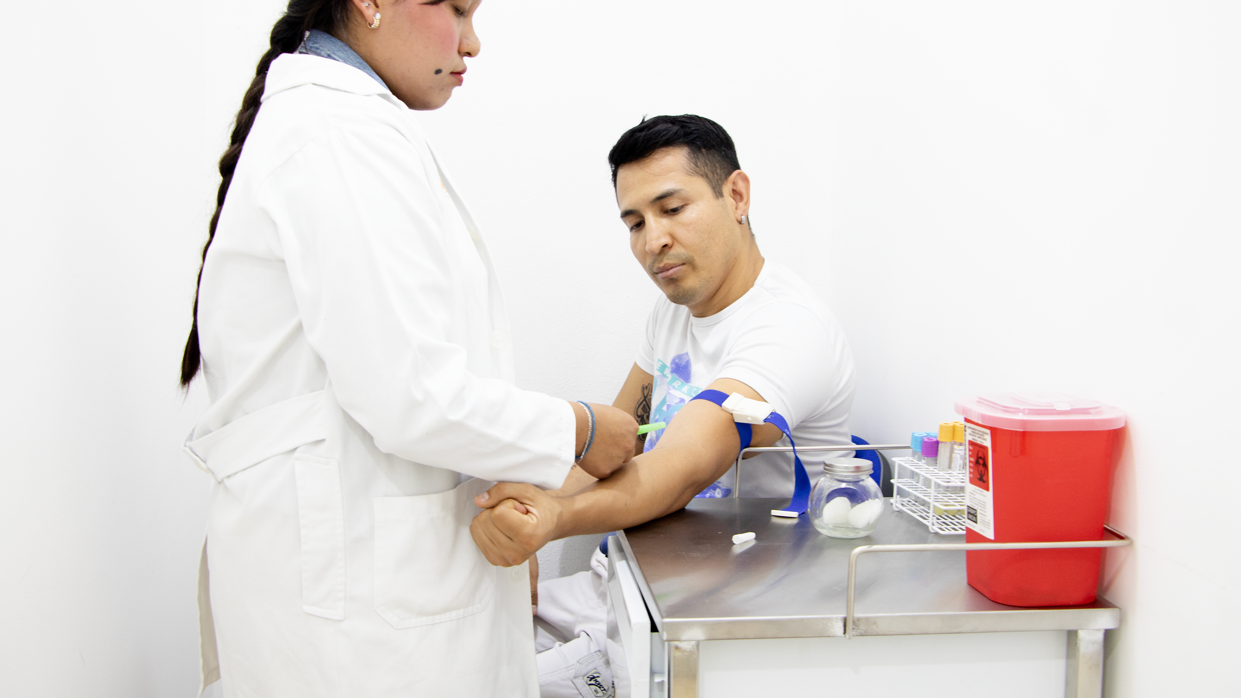 A healthcare professional drawing blood from a male patient in a medical clinic, with tubes and medical supplies on the counter.