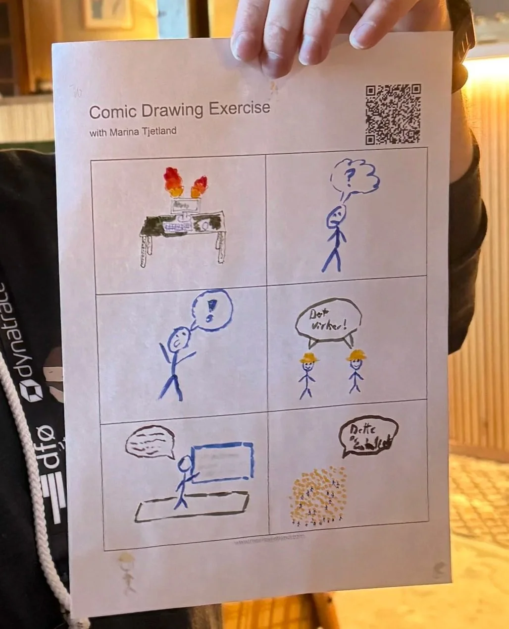 A hand holding a comic drawing exercise sheet with six illustrations and text, including a burning desk, a person with a question mark, a person with an exclamation mark, two workers saying 'Dajte vreme!', a person watching TV, and a speech bubble wi