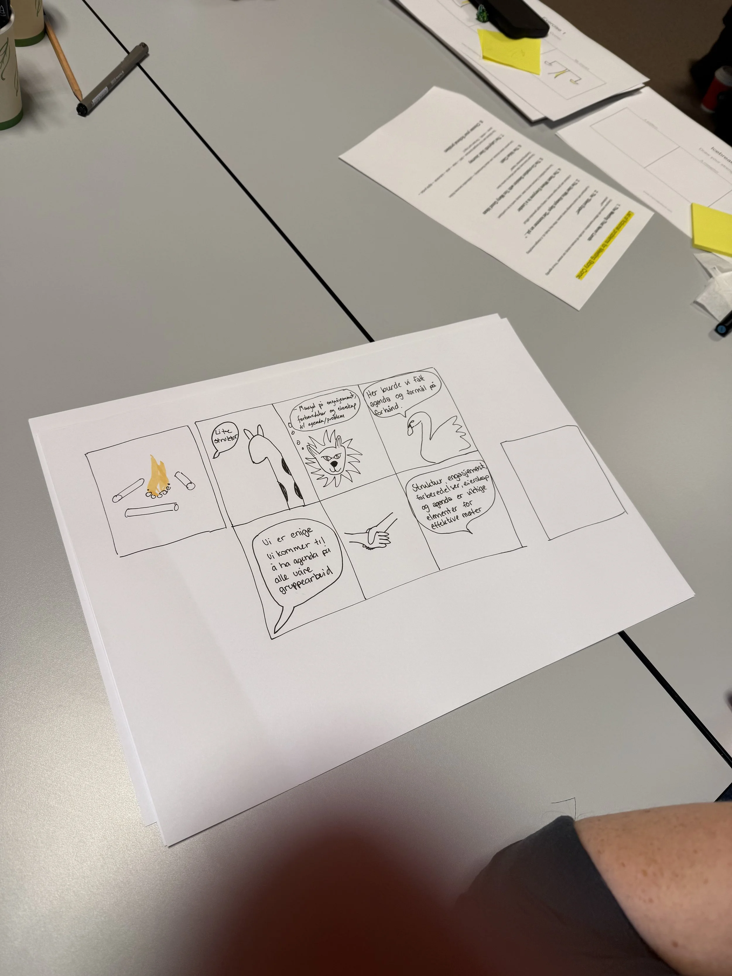 A table with documents, including a comic strip, and a pen, in an office or meeting room setting.
