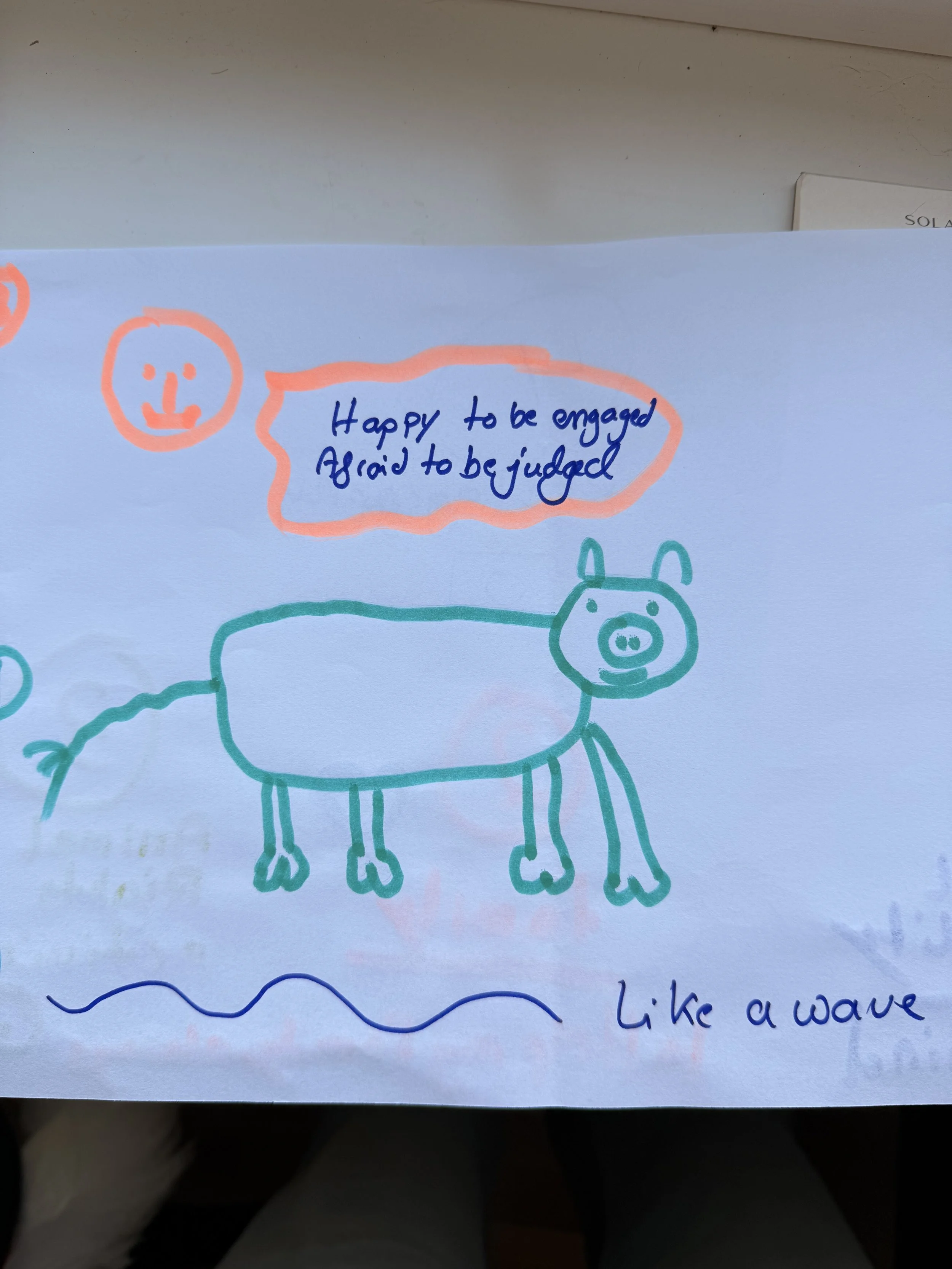 A child's drawing of a pig with four legs, a curly tail, and a smiling face. There is a speech bubble with a message saying, 'Happy to be engaged, afraid to be judged,' and the drawing is captioned 'Like a wave' at the bottom.