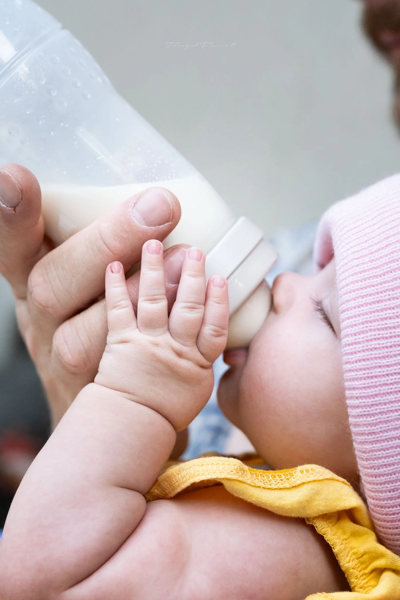 A baby drinking milk from an adult's hand.