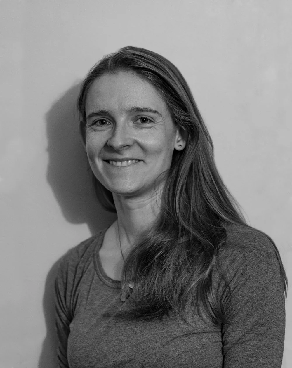 Black and white portrait of a smiling woman with long hair, wearing a t-shirt, against a plain background.