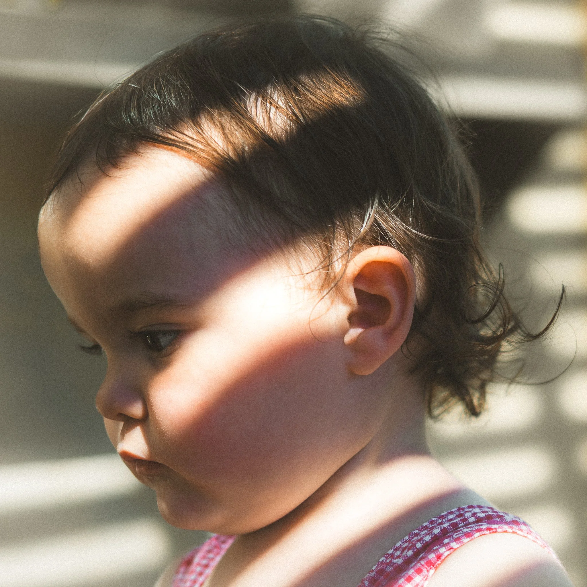 Close-up of a child's head with dark, curly hair and a fair complexion, and a small part of a pink and white patterned sleeve visible.