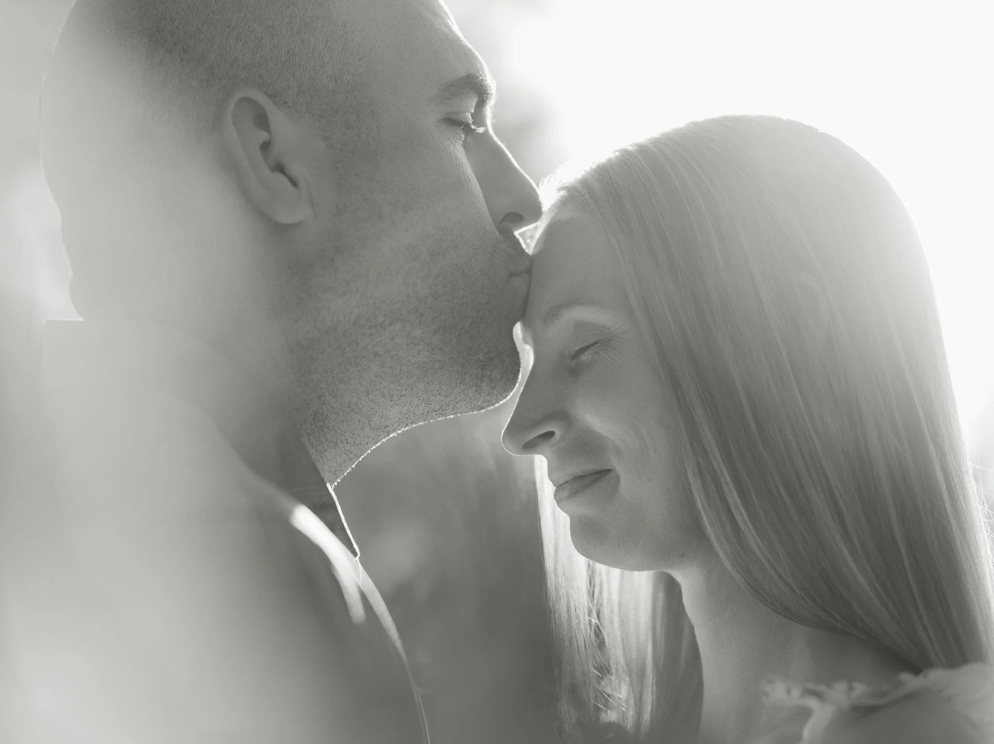 A close-up black and white photo of a man and woman gently touching foreheads with their eyes closed, conveying intimacy and affection.