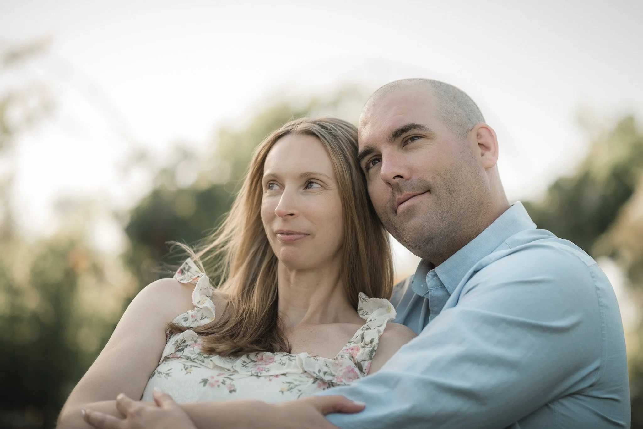 A close-up of a woman and a man outdoors, sitting and hugging over a blurred natural background.