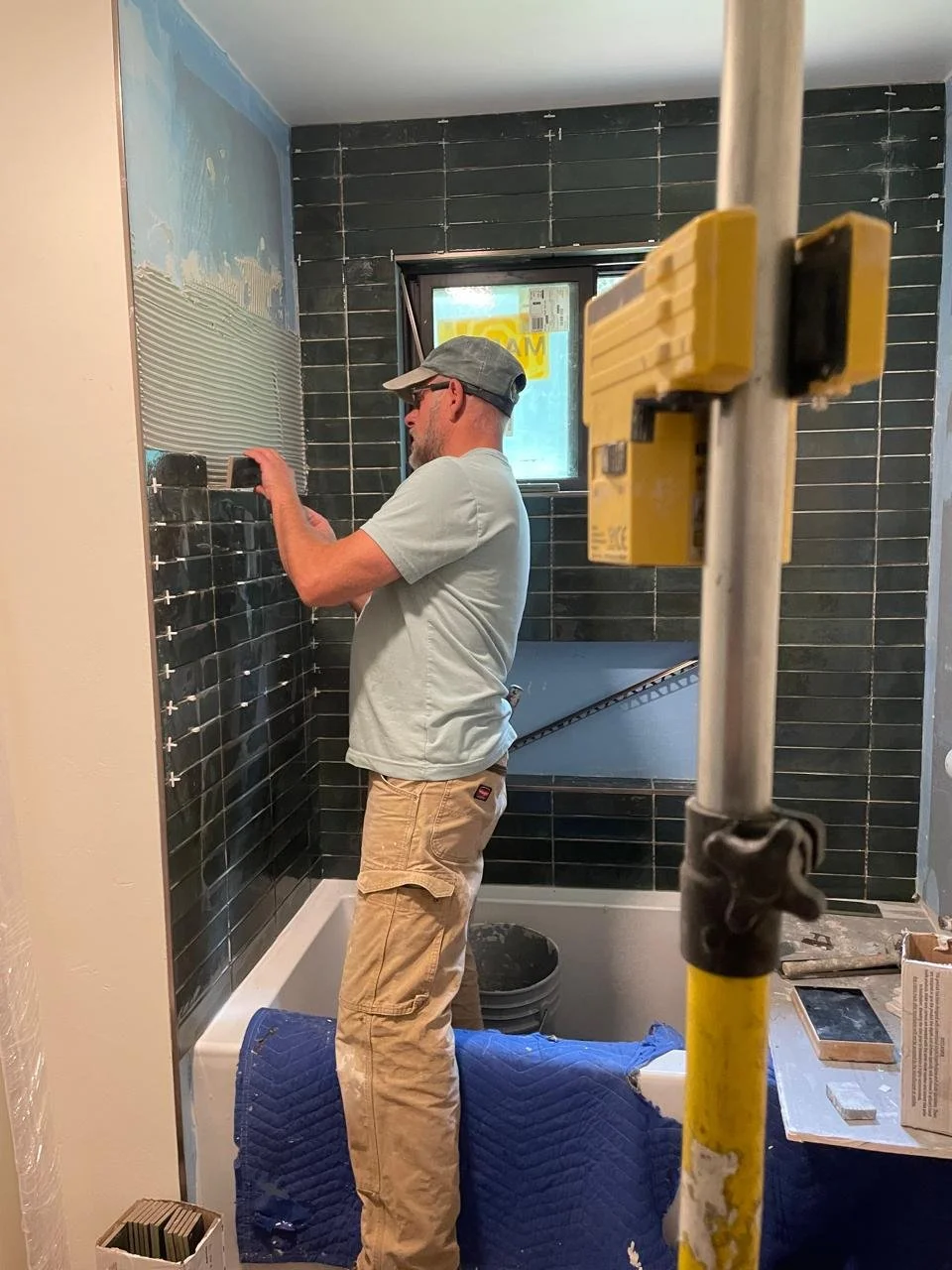 Professional tile installer installing dark green subway tile on a custom bathtub surround during a bathroom remodel in the Lake Tahoe area.