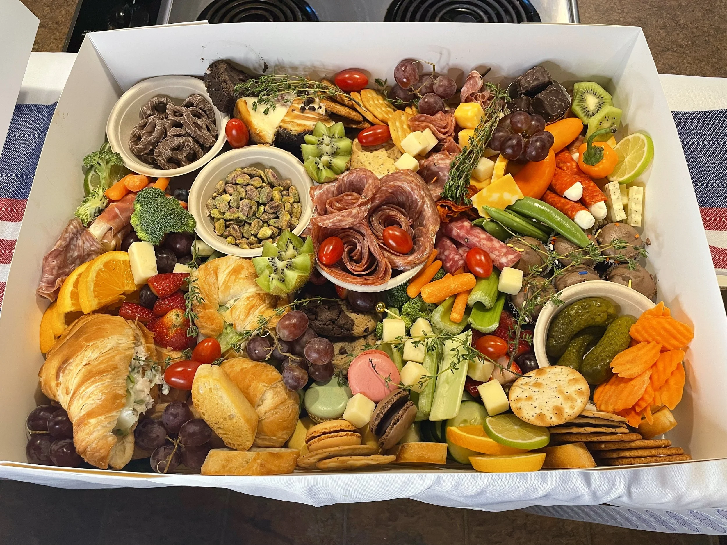 A large white tray containing a variety of fresh fruits, vegetables, cheese, crackers, chocolates, and small bowls of nuts and dips, suitable for a party platter or grazing table.