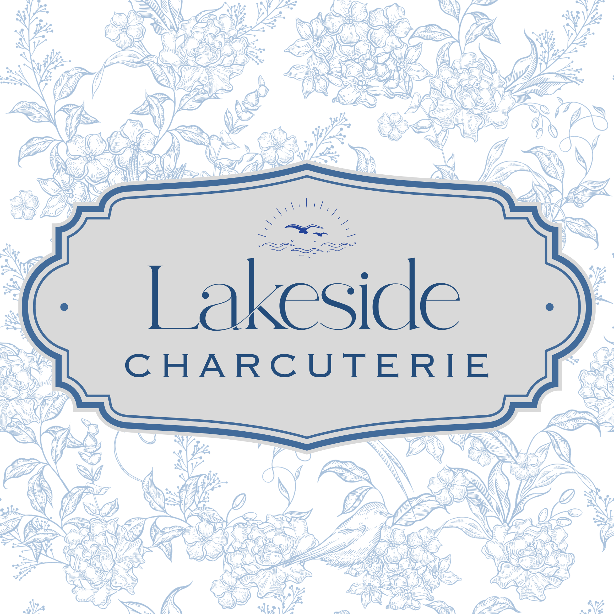 The image shows the label for a charcuterie product from Lakeside, featuring a floral background with blue line art of various flowers and leaves. The label includes a stylized illustration of a seagull flying over water with a sun in the background.