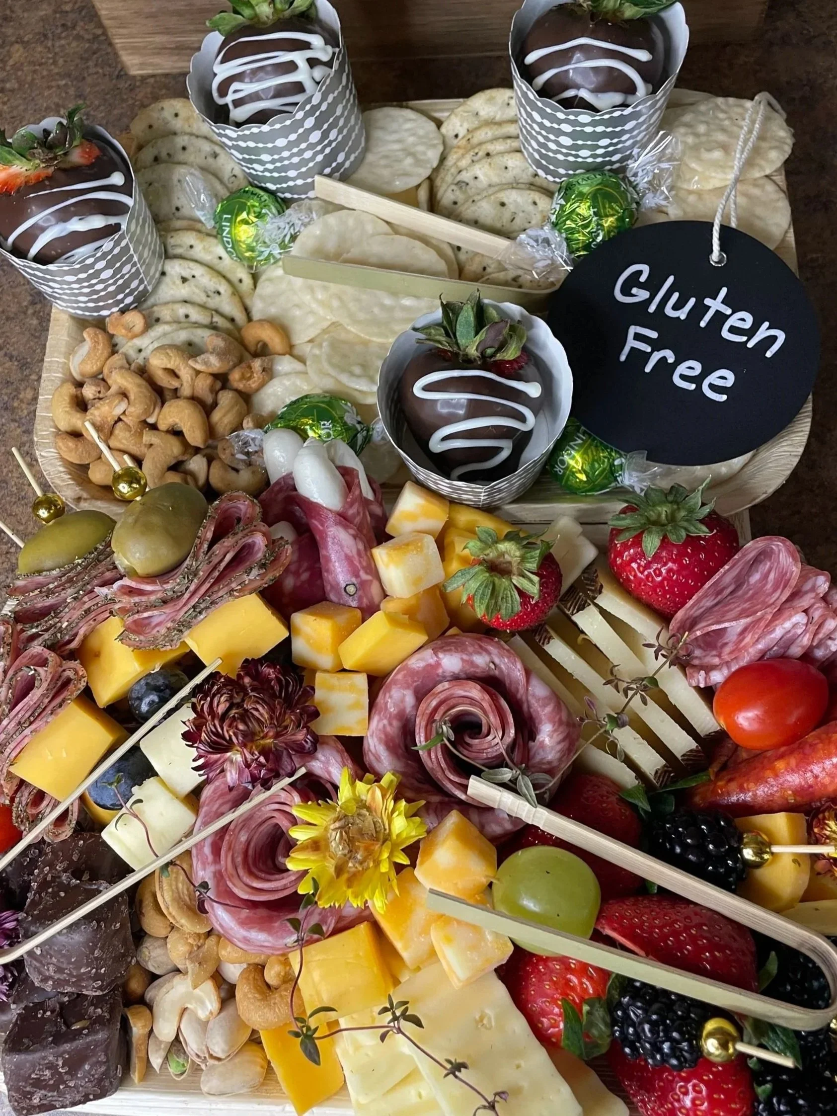 Assorted cheese, fruits, nuts, chocolates, and charcuterie on a platter with a 'Gluten Free' sign.
