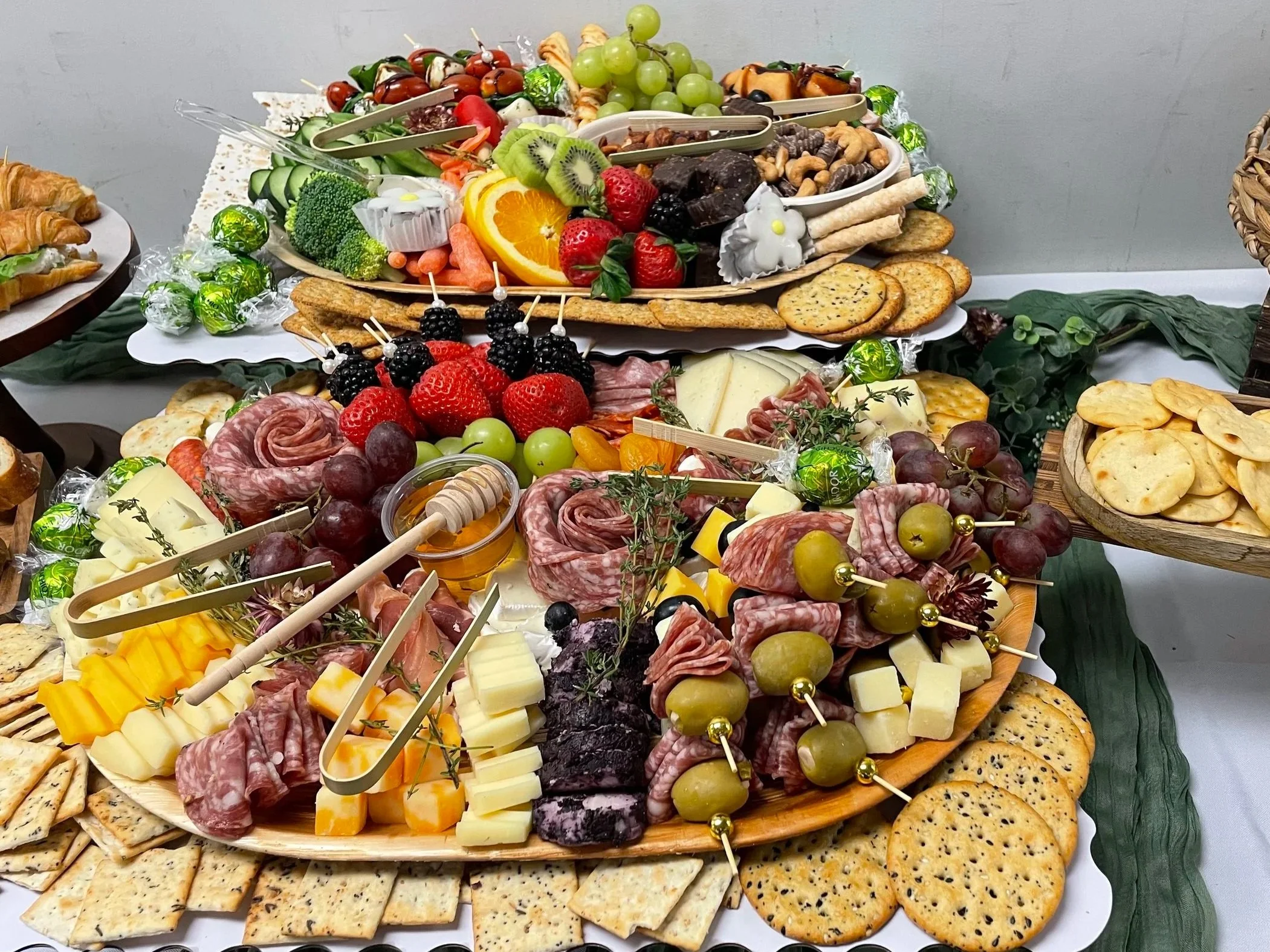 A large, multi-tiered platter with an assortment of fresh fruit, cheeses, crackers, charcuterie, nuts, and candies, arranged for a party or celebration.