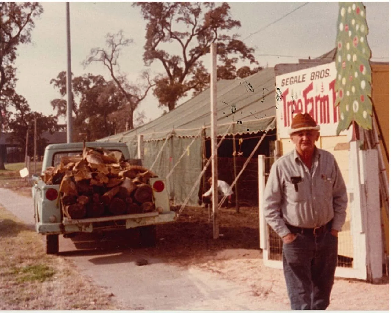 A man standing outdoors next to a sign for fresh cut christmas trees