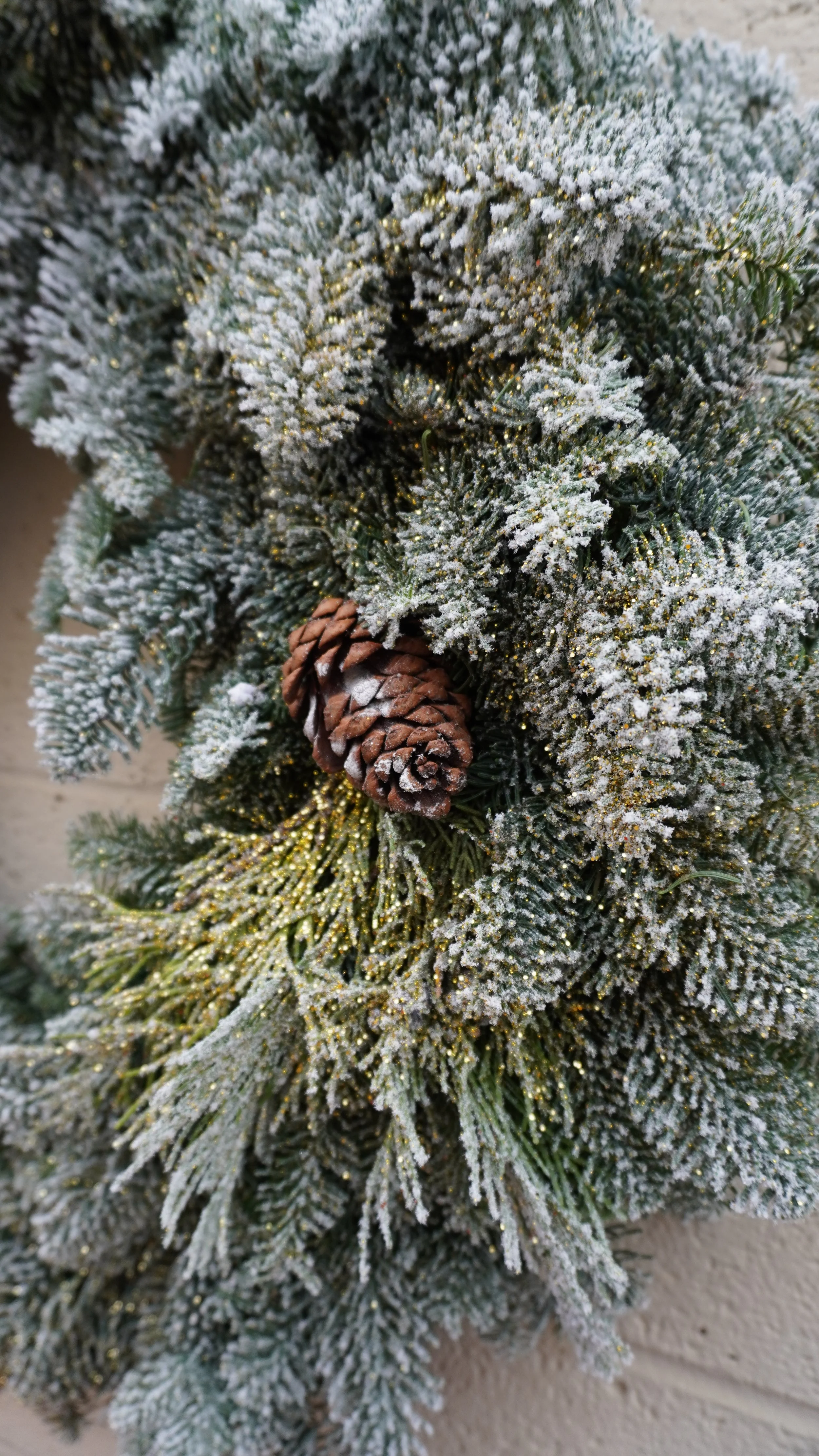 A close-up of an flocked Christmas tree branch covered in snow and decorated with a pine cone.
