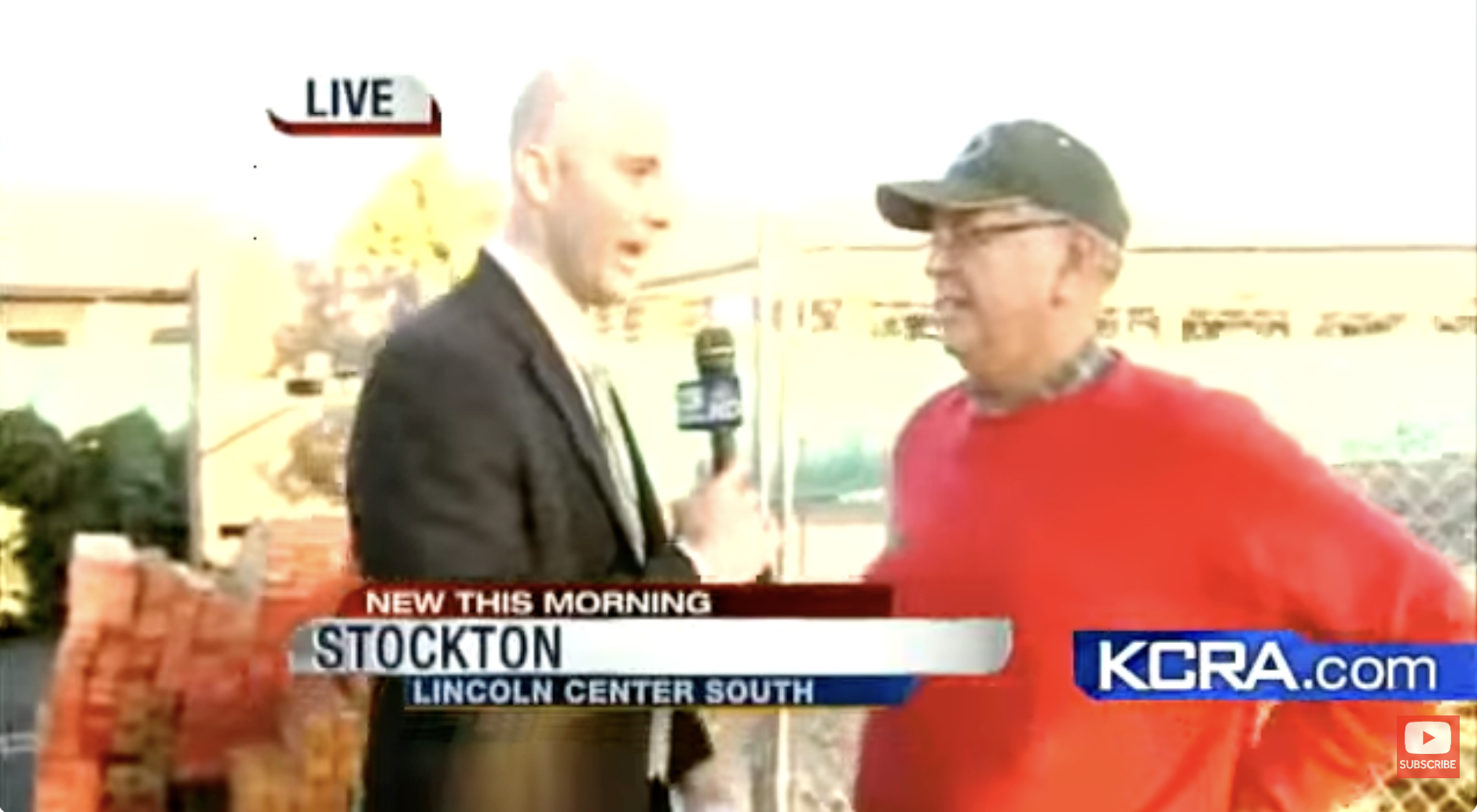 News reporter with a microphone interviewing a man in a red shirt and cap outdoors, with a shopping cart filled with bricks nearby, during a live broadcast for KCRA in Stockton.