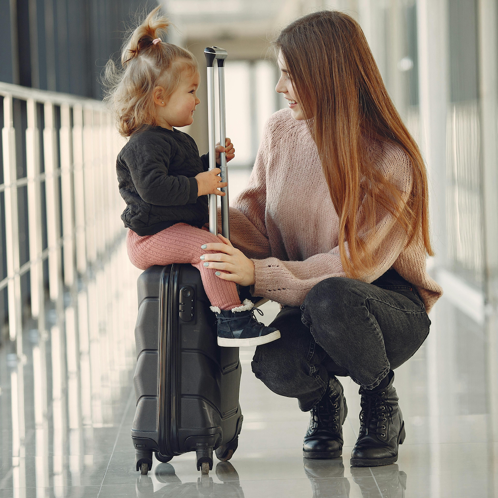 A woman kneeling next to a small girl sitting on a suitcase, representing a link to the Adoption Dossier Apostille page