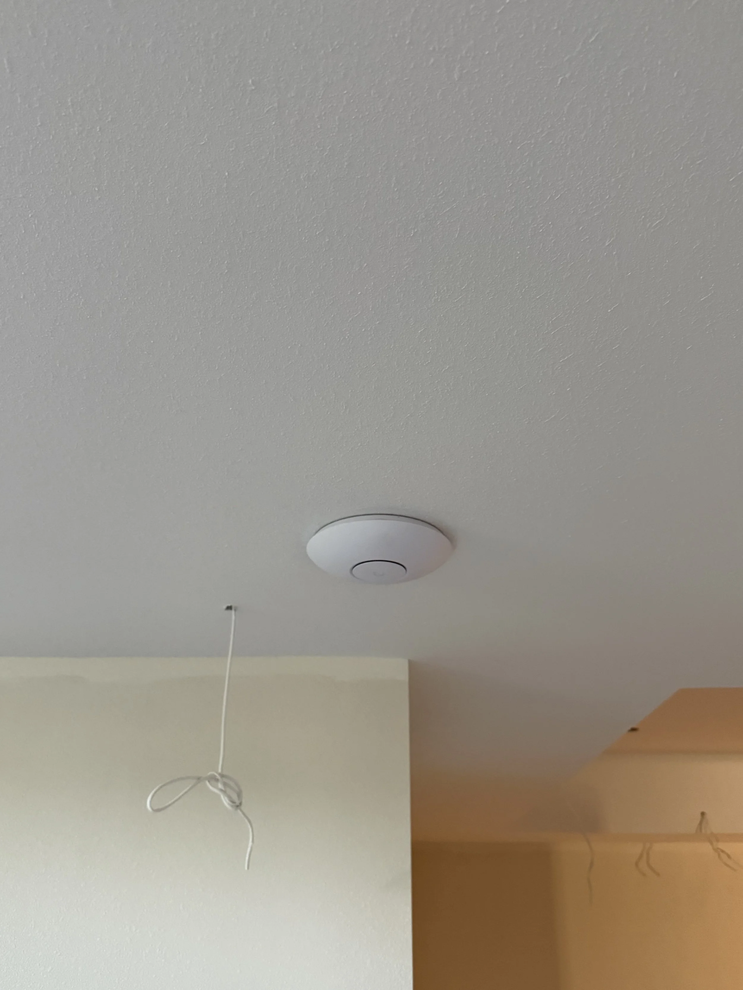 Ceiling with a smoke detector, a light fixture, and a hanging wiring loop. The ceiling has two different colors/divisions, with the junction at the middle. The right side is brown, and the left side is beige.