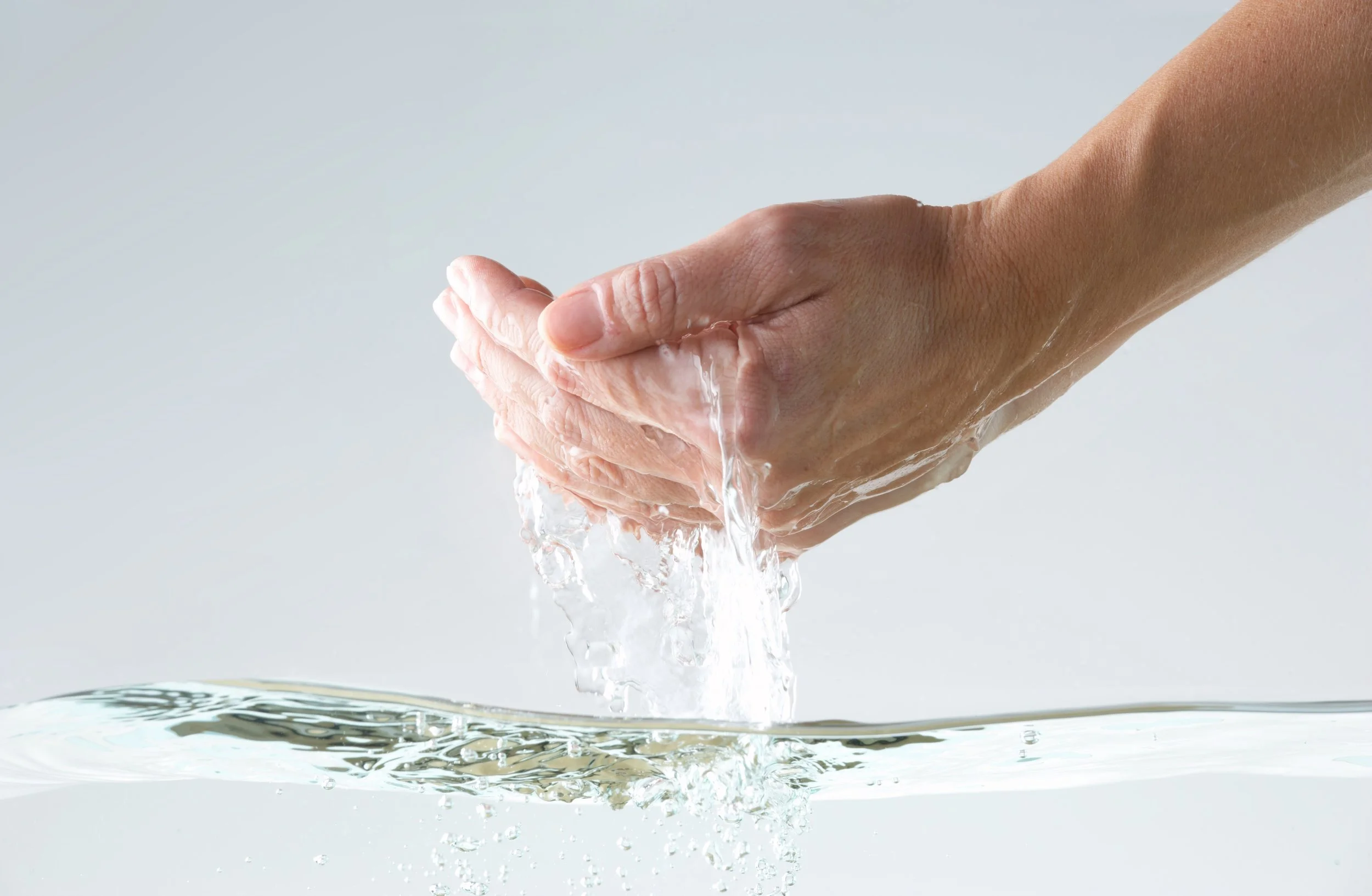 A hand is washing under running water, with water splashing and flowing into a sink.
