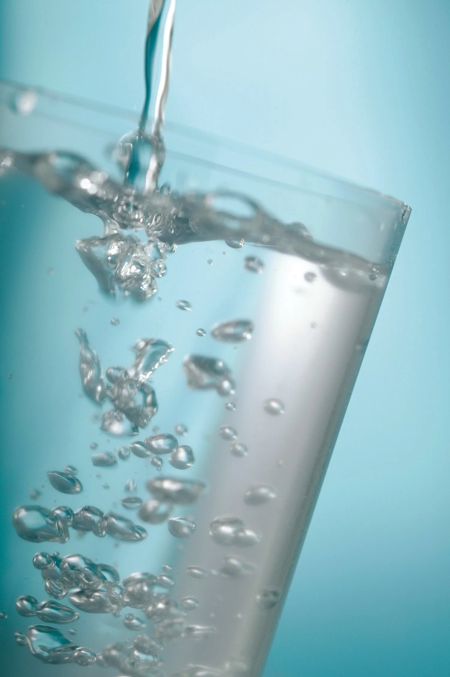 Close-up of water being poured into a transparent glass against a light blue background.