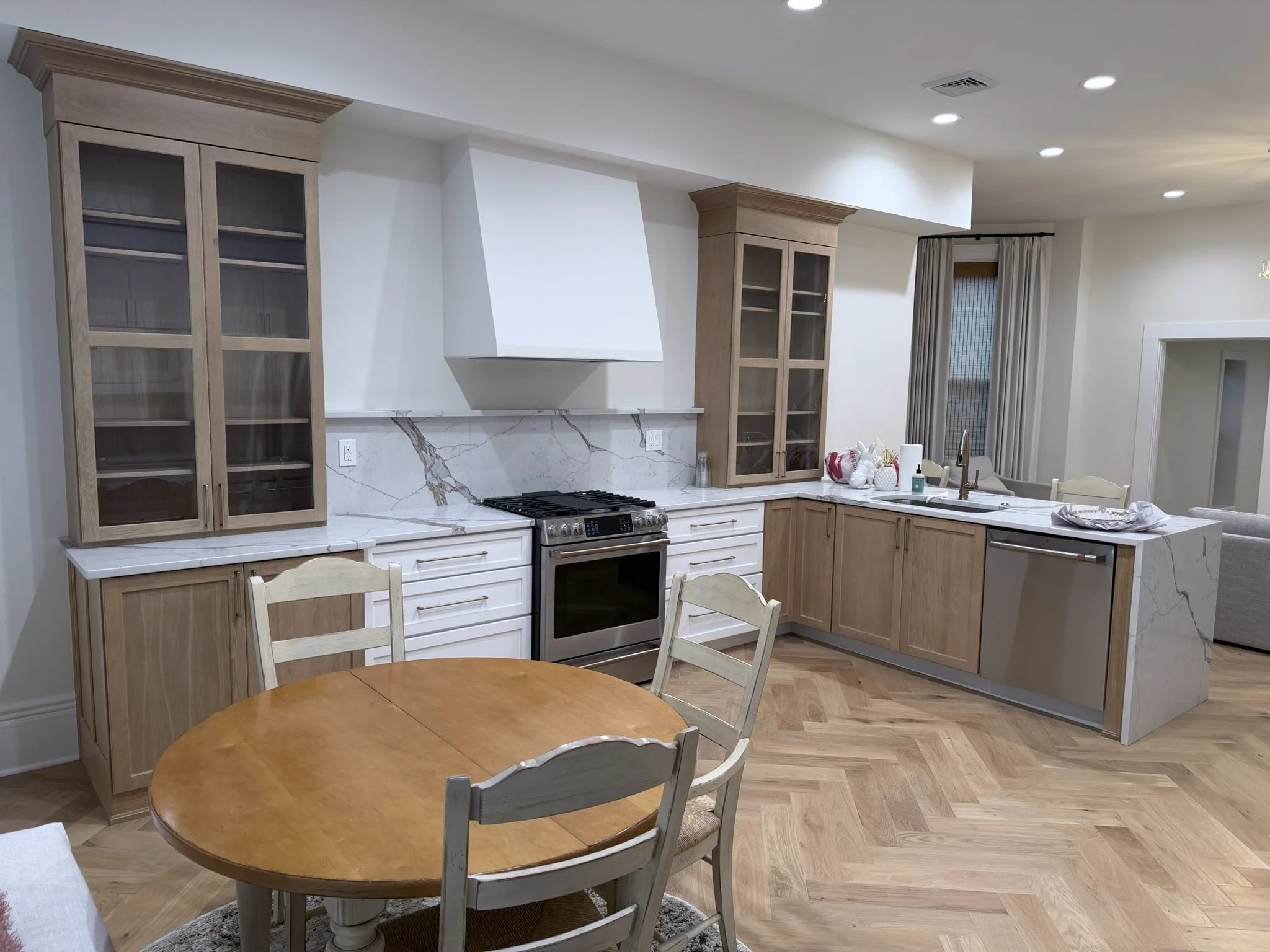 Open kitchen with wooden cabinets, marble countertops, a stove, and a round dining table with chairs.