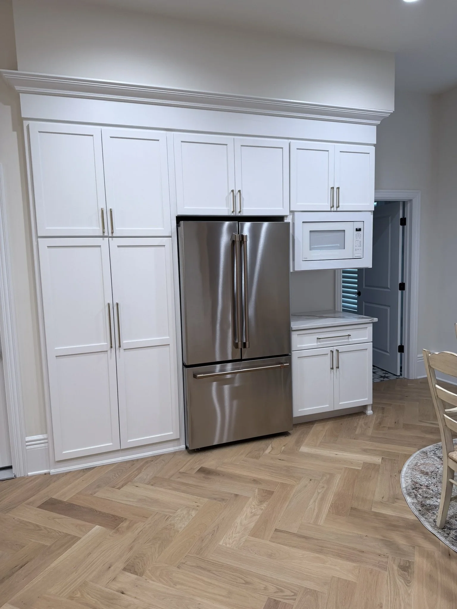 Kitchen with white cabinets, stainless steel refrigerator, microwave, and herringbone wood flooring.