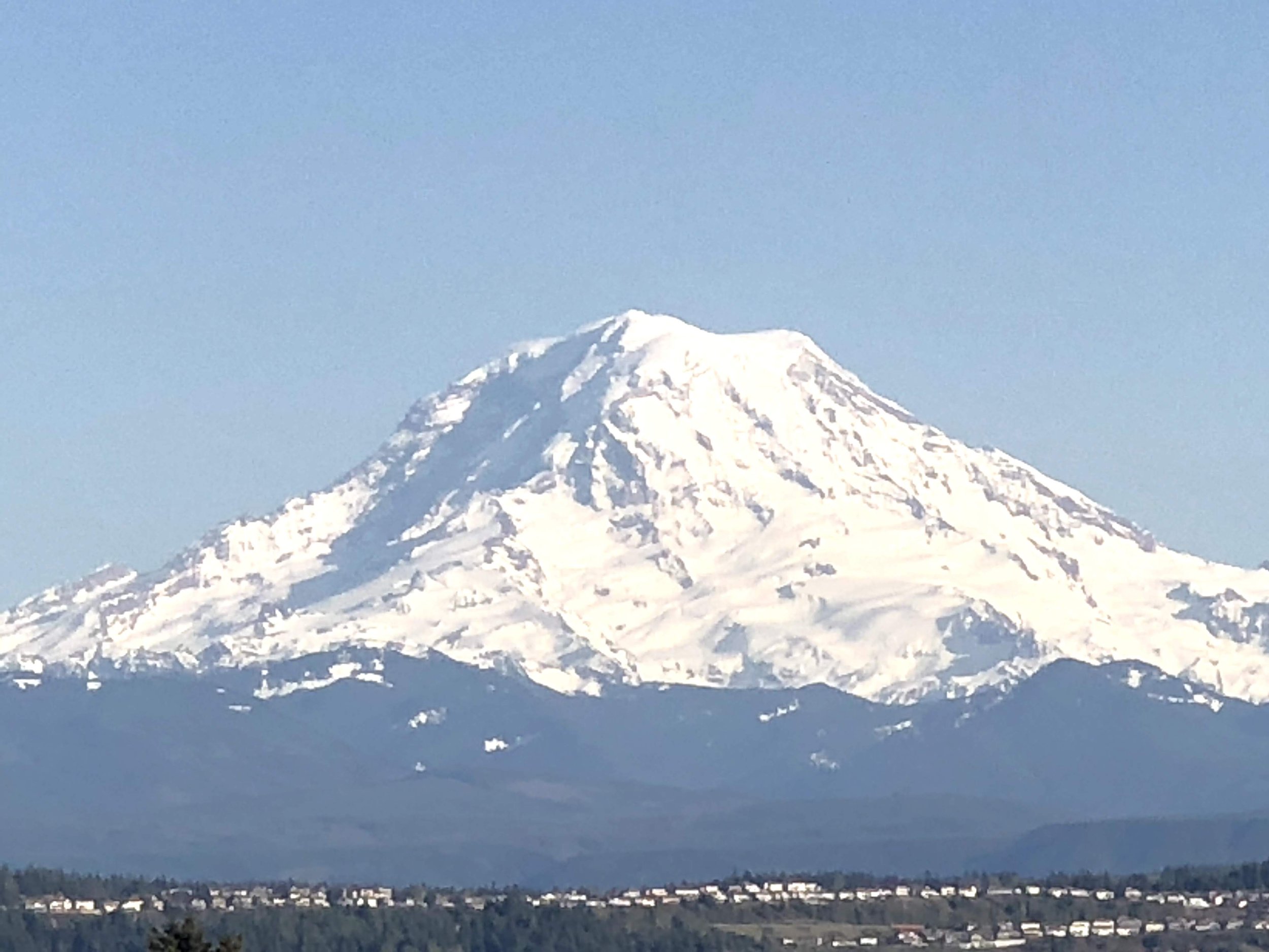 Snow-capped mountain in the distance under a blue sky, with a small town or city at the base and a field in the foreground.
