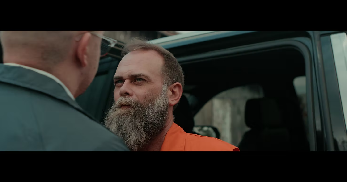 A man in an orange jumpsuit looks angry