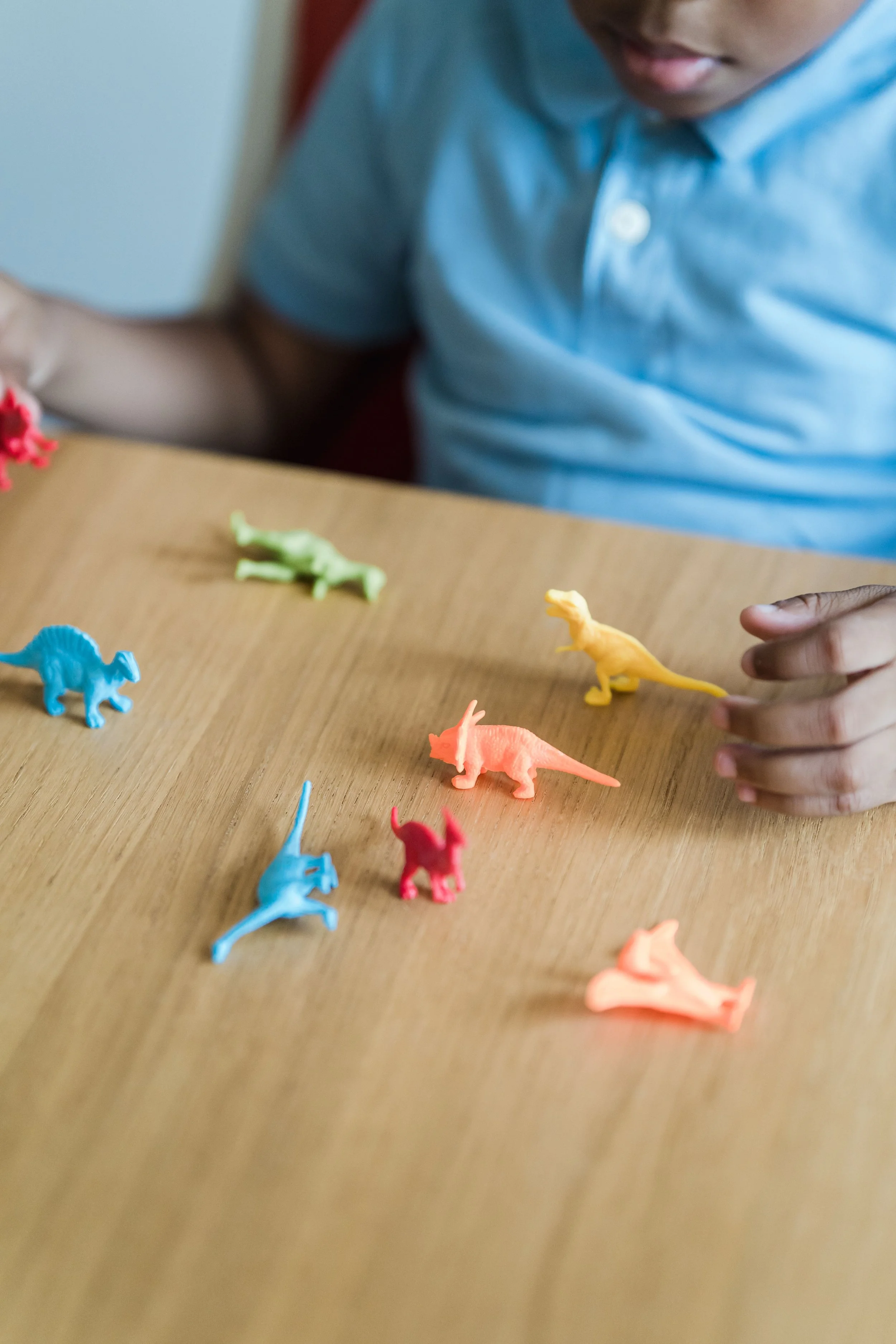 A child with dark skin plays with small colorful toy dinosaurs
