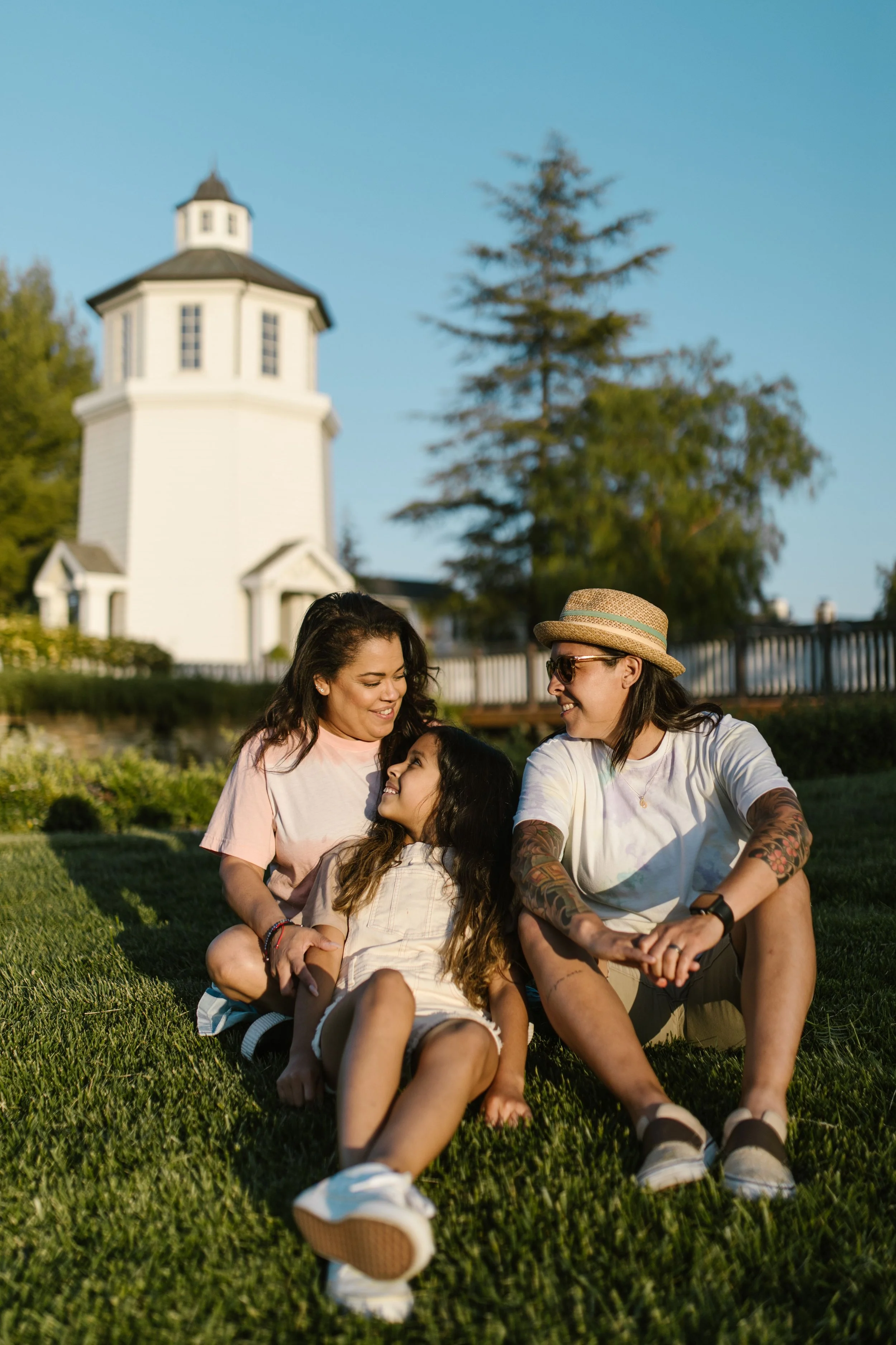 A smiling tan skinned family: two moms and a child with long hair.