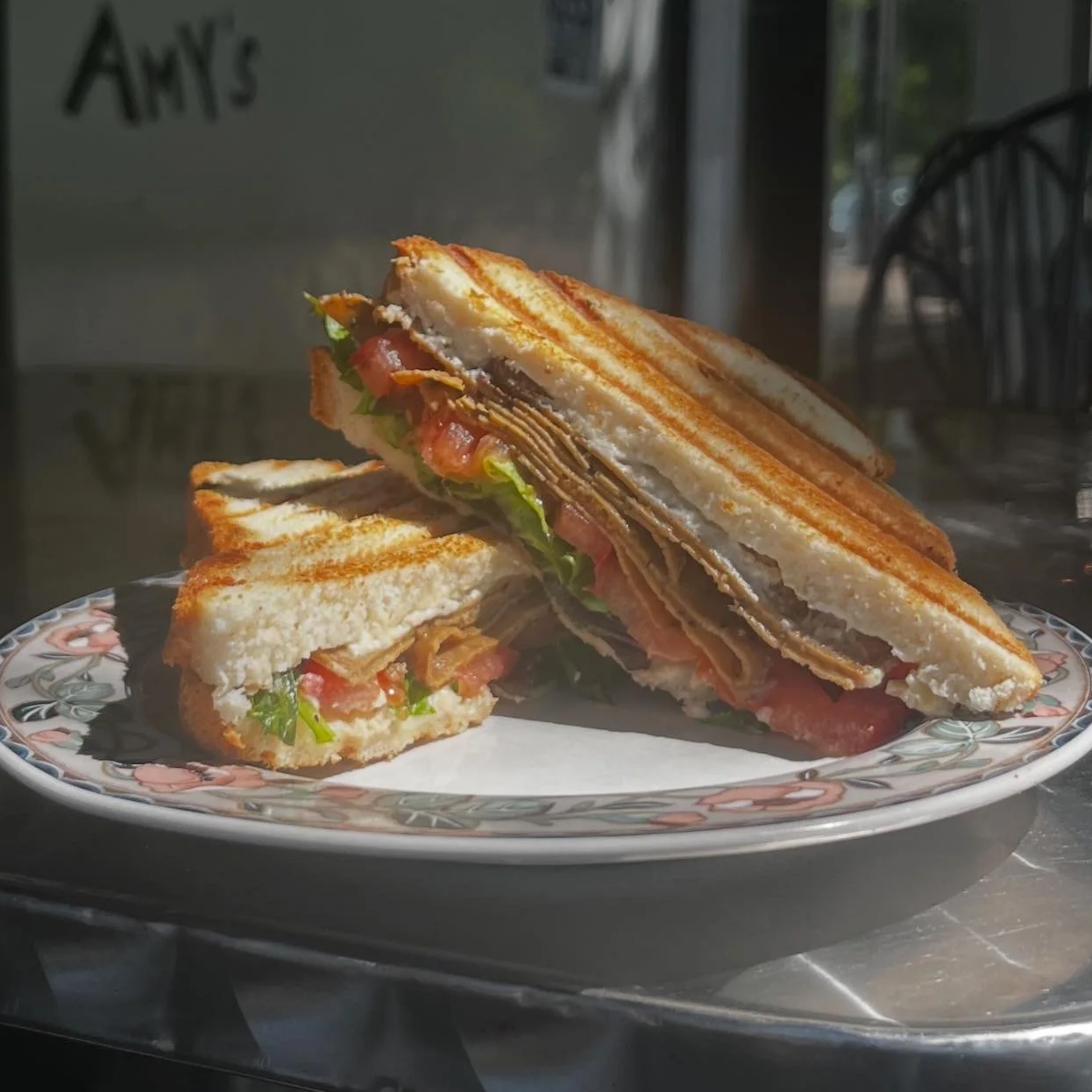 A plate with a toasted sandwich cut in half, filled with bacon, lettuce, tomato, and cheese.