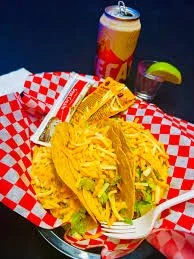 Fried fish tacos with lettuce and sauce on a checkered paper with a drink in the background The Easy Inn Kansas Citys best kept secret underground dive bar serving great bar food