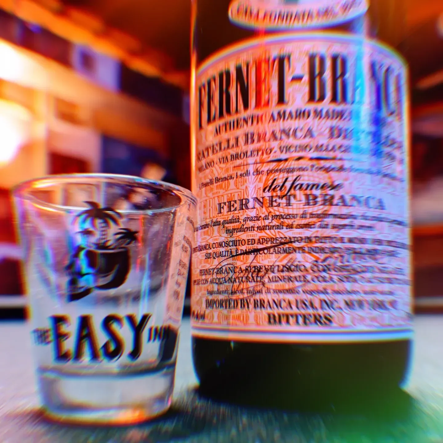 A bottle of Fernet with detailed label and a small glass of Fernet shot with a palm tree logo at The Easy Inn Kansas Citys best kept secret underground dive bar serving great bar food with a staff that makes this place unforgettable.