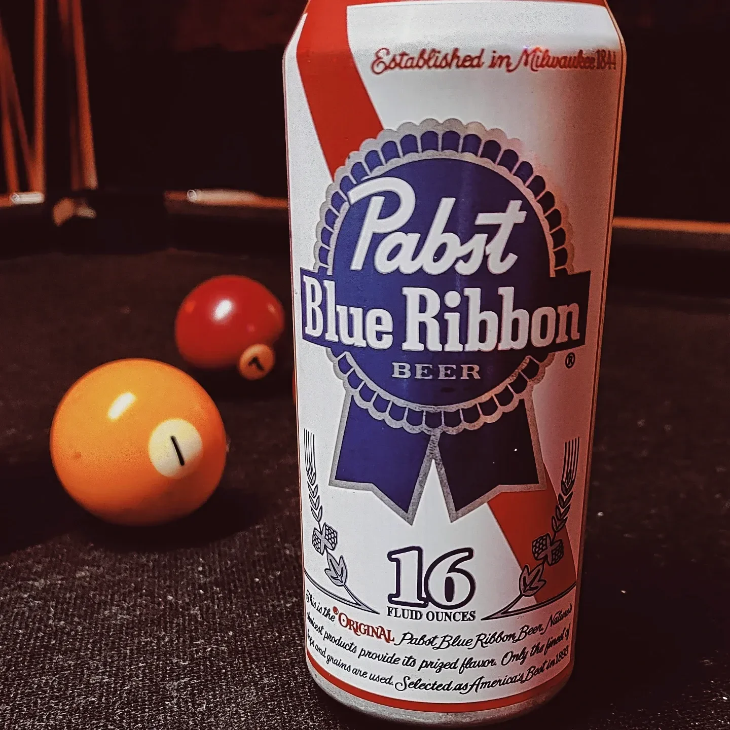 A can of Pabst Blue Ribbon beer on a dark surface with two billiard balls, a red one and a yellow one, in the background The Easy Inn Kansas Citys best kept secret underground dive bar serving great bar food