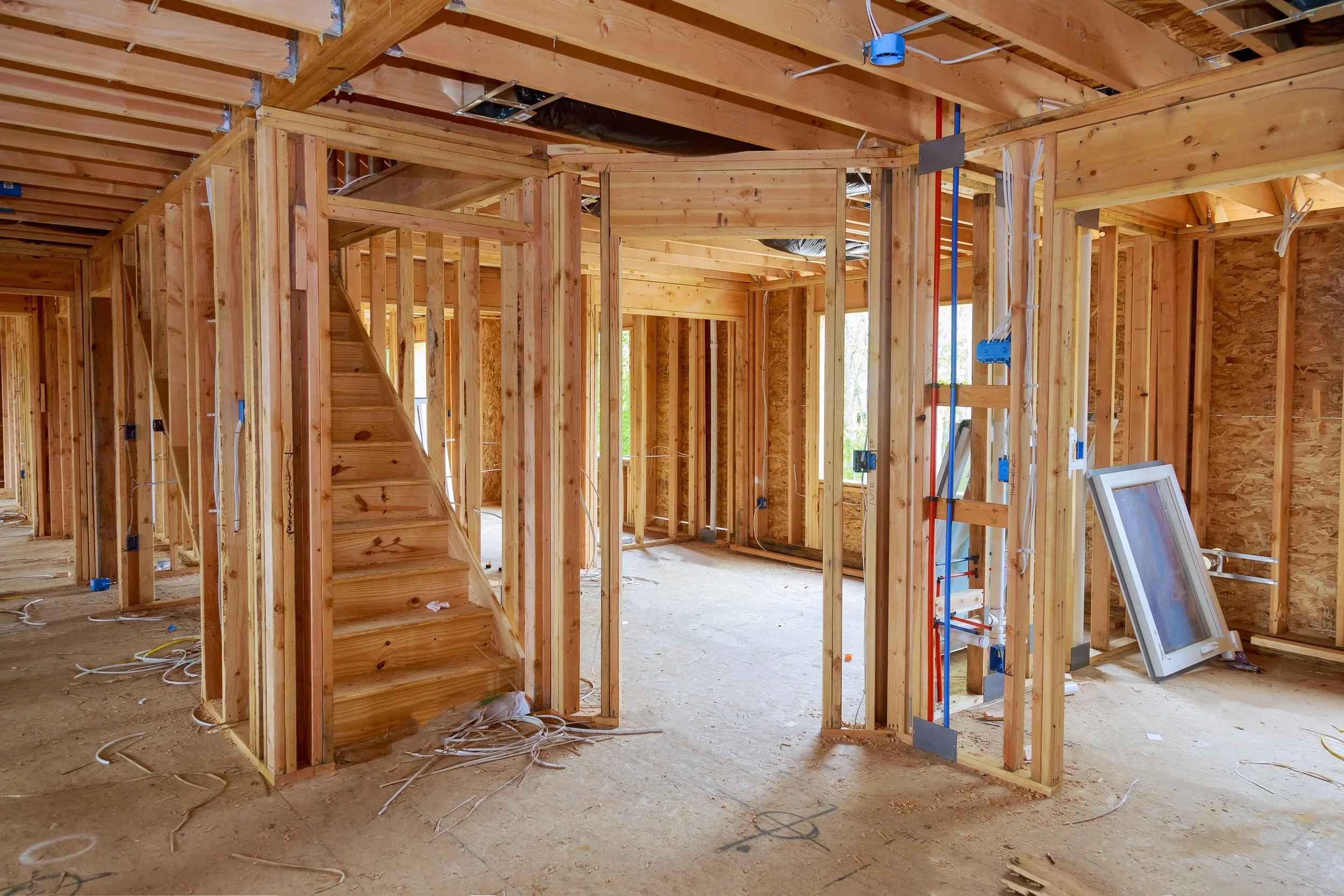 Interior view of a house under construction with exposed wooden framing, staircase, and electrical wiring.