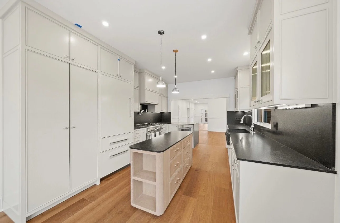 Modern kitchen with white cabinets, black countertops, a small island, hardwood flooring, and recessed lighting.