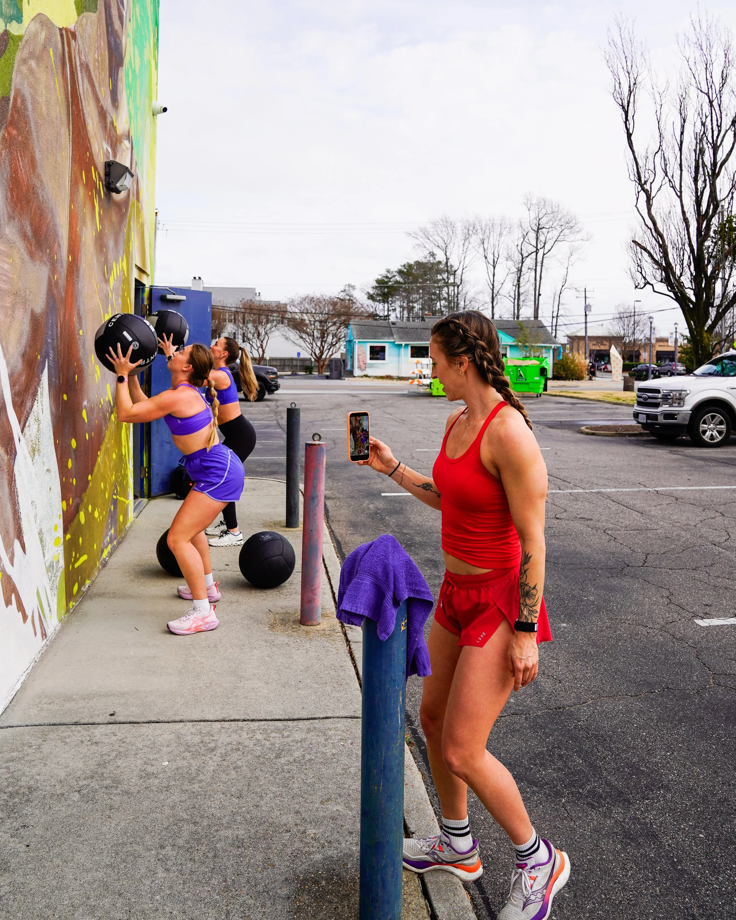 Women working out with medicine balls against a colorful outdoor wall during daytime.