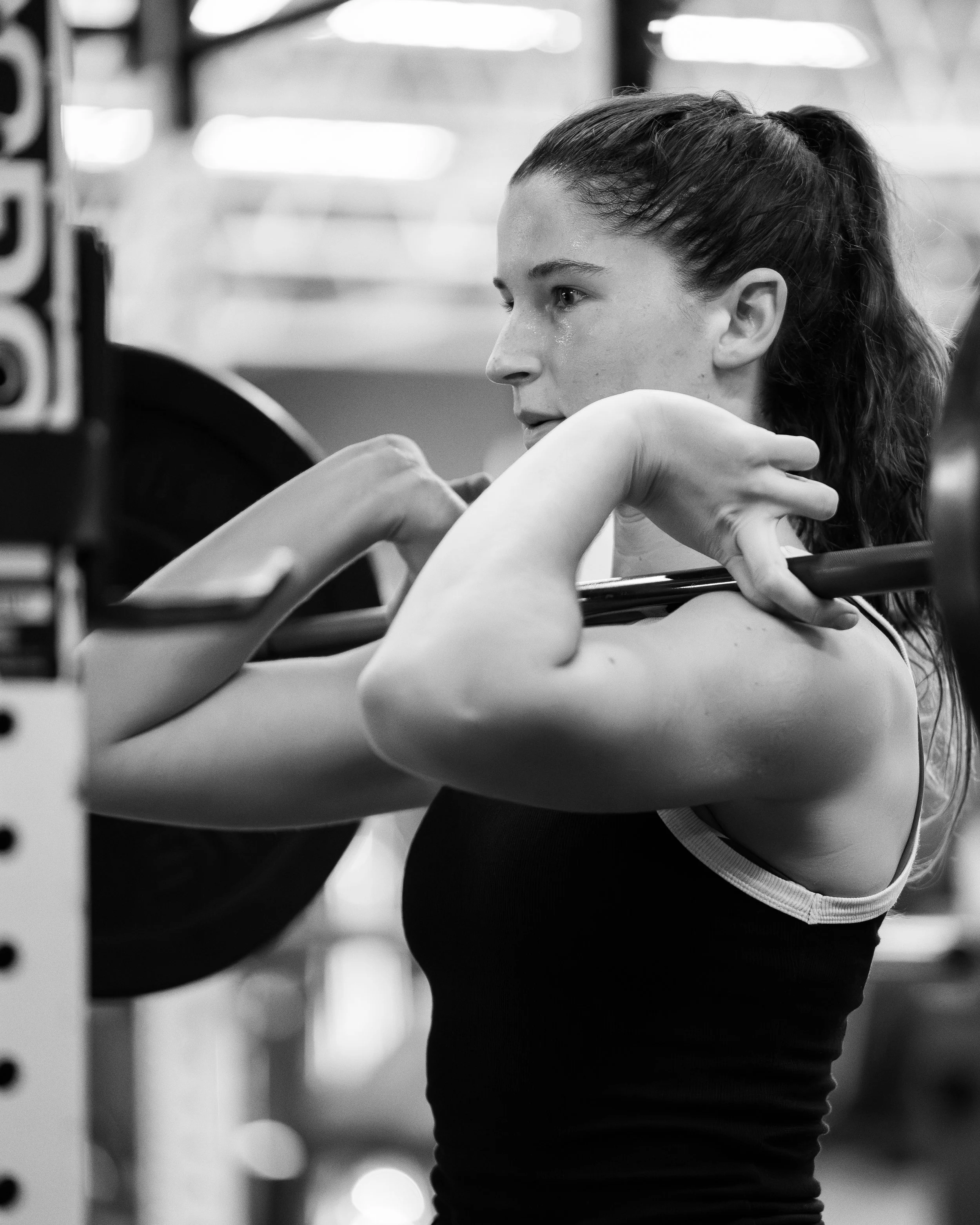 A woman with wet hair and sweat on her face, dressed in sporty attire, is reaching through gym equipment in a fitness setting.