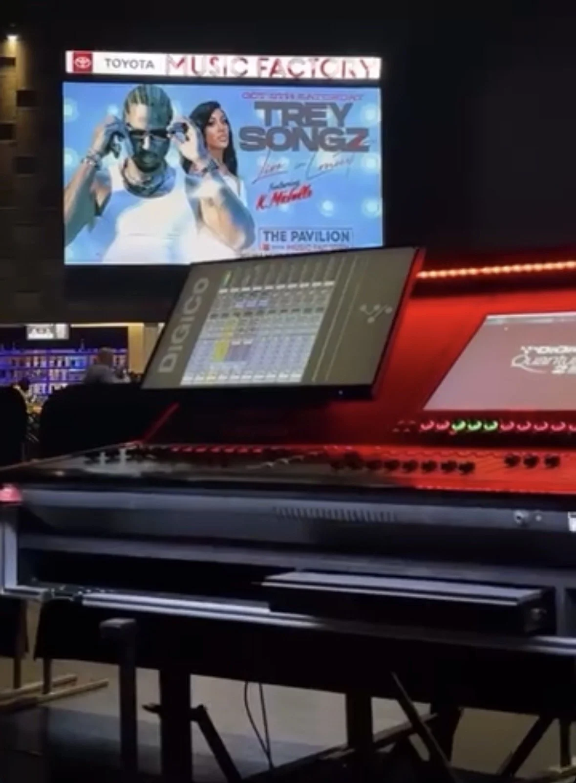 A Digico 225 console setup with two screens in an amphitheater. The upper screen displays a promotional poster for Trey Songz's concert, featuring images of Trey Songz and K Michelle, with event details. The lower screen shows a digital audio