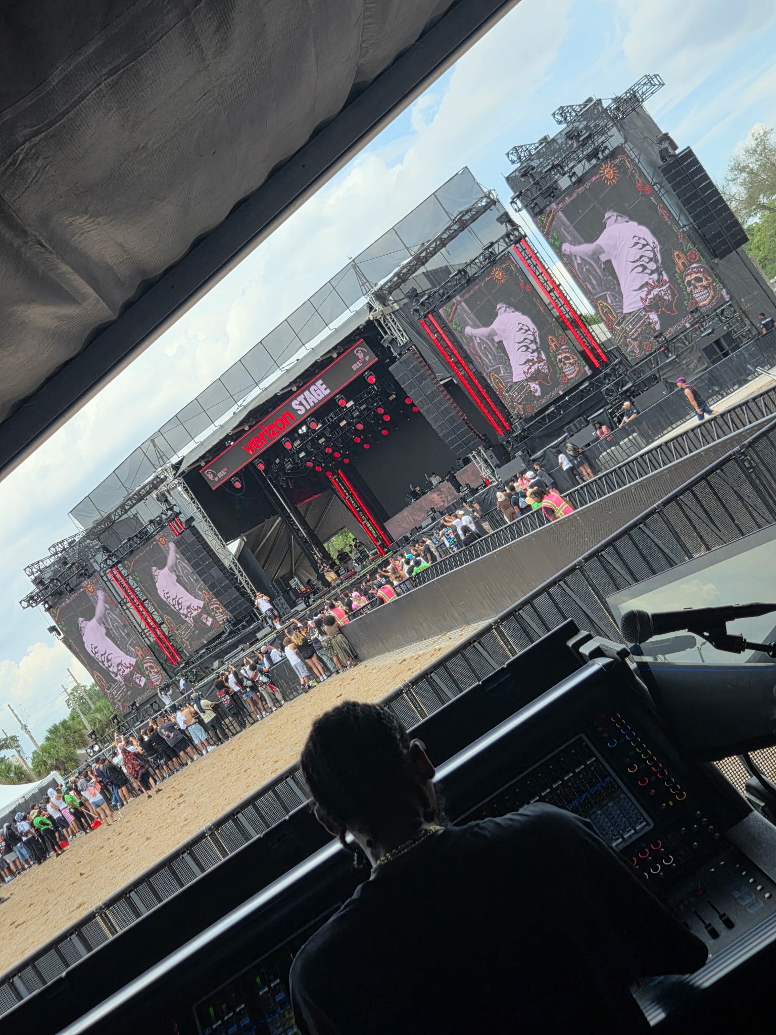 OC Chris at Rolling Loud Orlando 26'. View of an outdoor concert stage with large screens, stage lights, and a crowd of people. Engineer on a Digico console with a DJ or performer in the foreground.