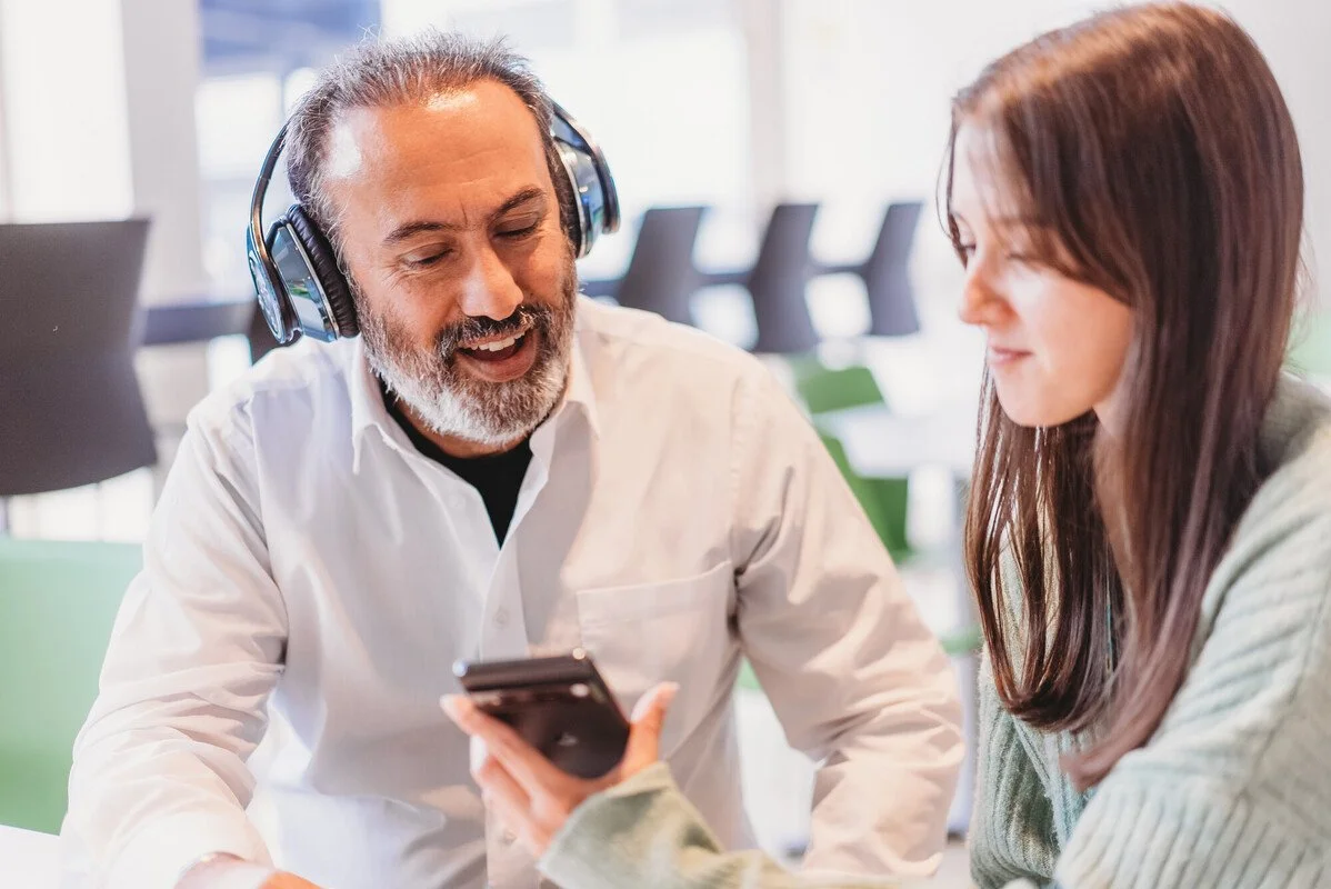 Person with less-visible disabilities wears headphones to listen to audio on phone with friend or work colleague