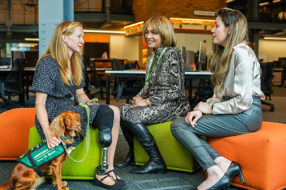 Person with limb loss and assistance dog meets with colleagues in casual seating area
