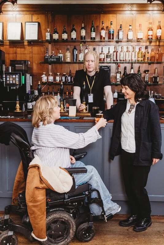 Person with albinism serves two customers at a bar (one has multiple disabilities)