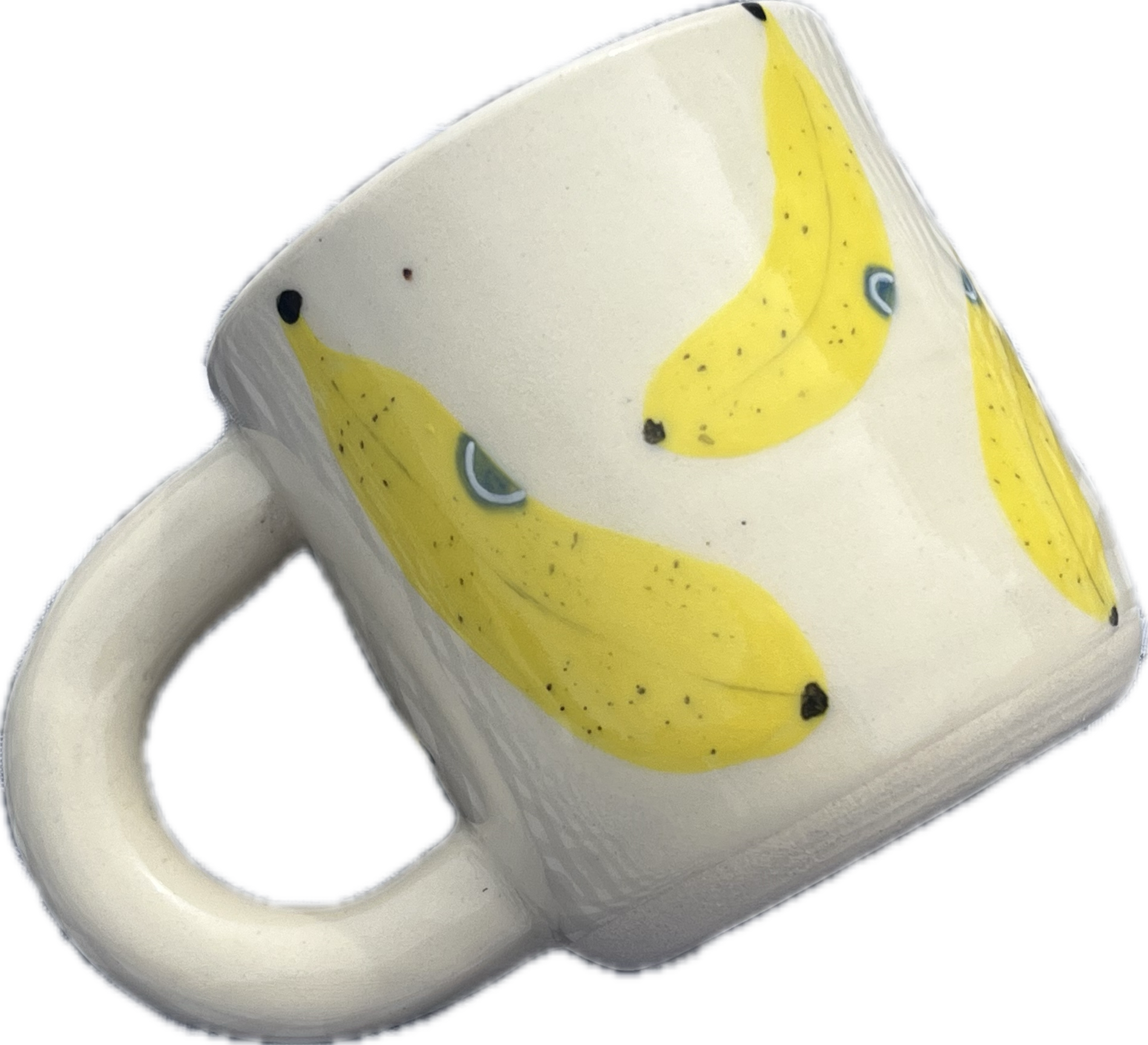 Close-up of a white ceramic mug with a yellow banana print and black dots on it, viewed against a black background.