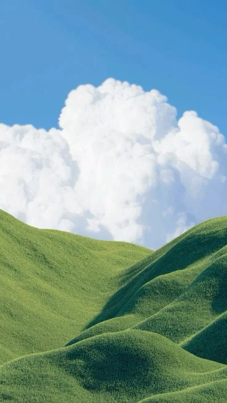 Green rolling hills under a bright blue sky with large white fluffy clouds.