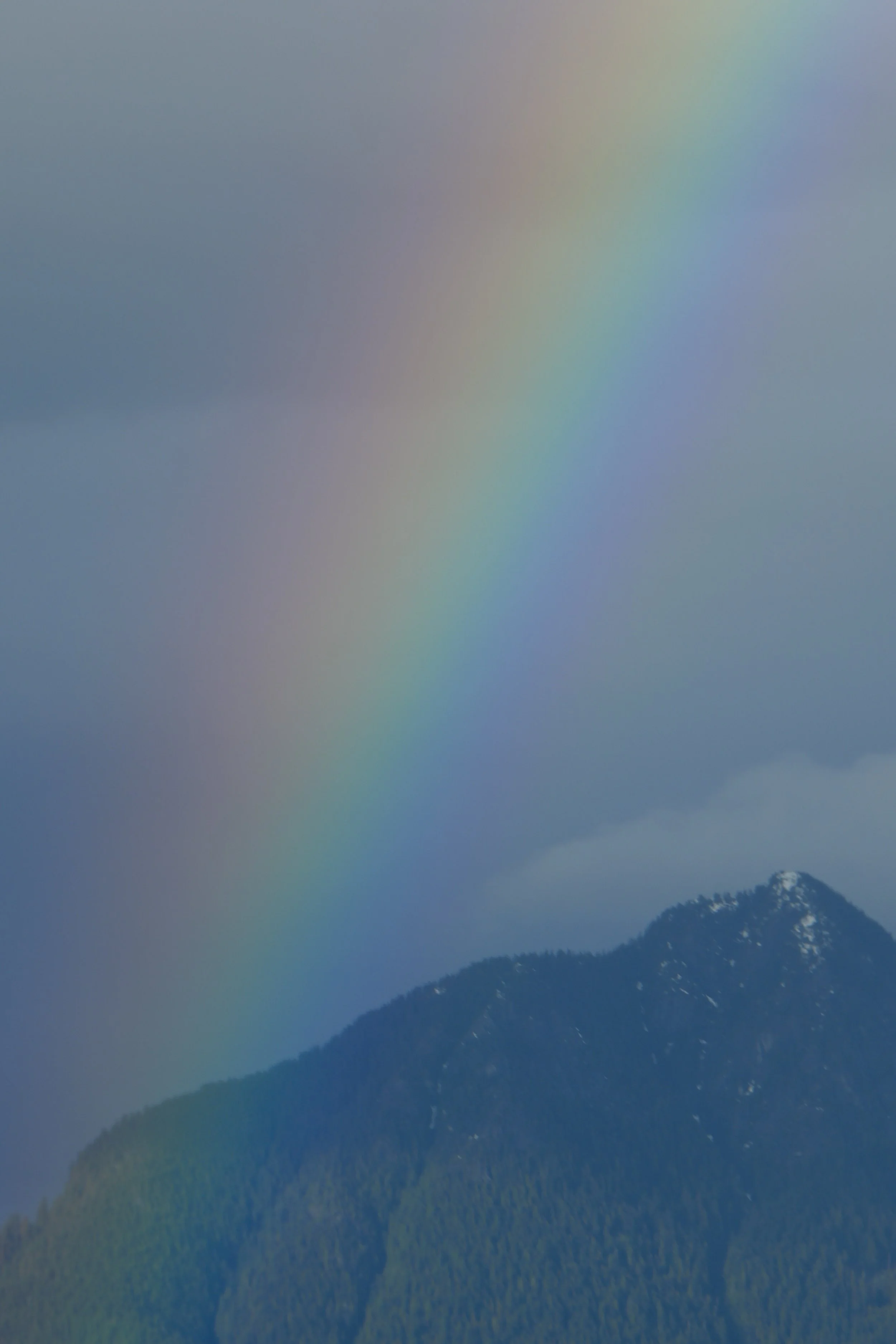 Mountain landscape with a colorful rainbow and overcast sky.
