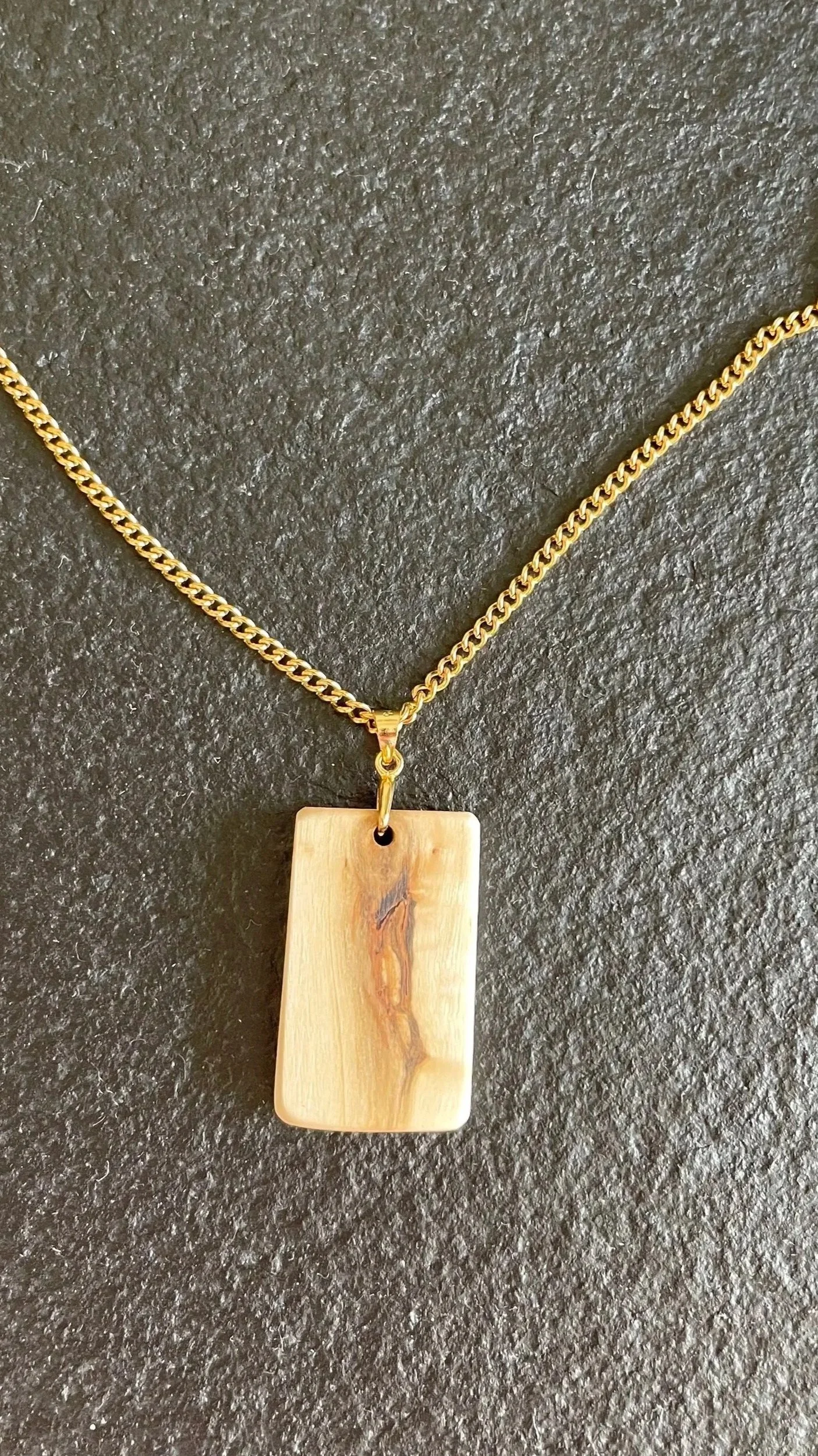 Gold chain necklace with a rectangular cream-colored pendant hanging from it, displaying natural wood grain patterns, made by Robert Seavy