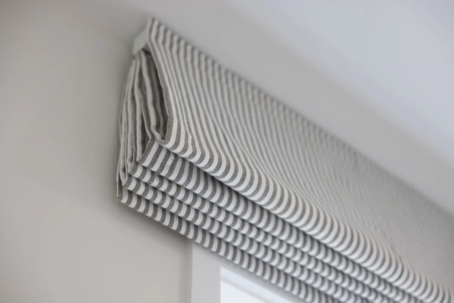 Gray and white striped fabric roman blind hanging fixed to the wall above a window