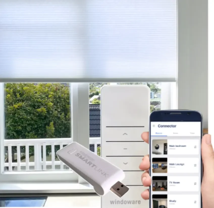 A smartphone displays a home automation app controlling various rooms, while a remote control and a small white device labeled "SMART LINK" are near a window with a white blinds, overlooking trees and a house roof outside.