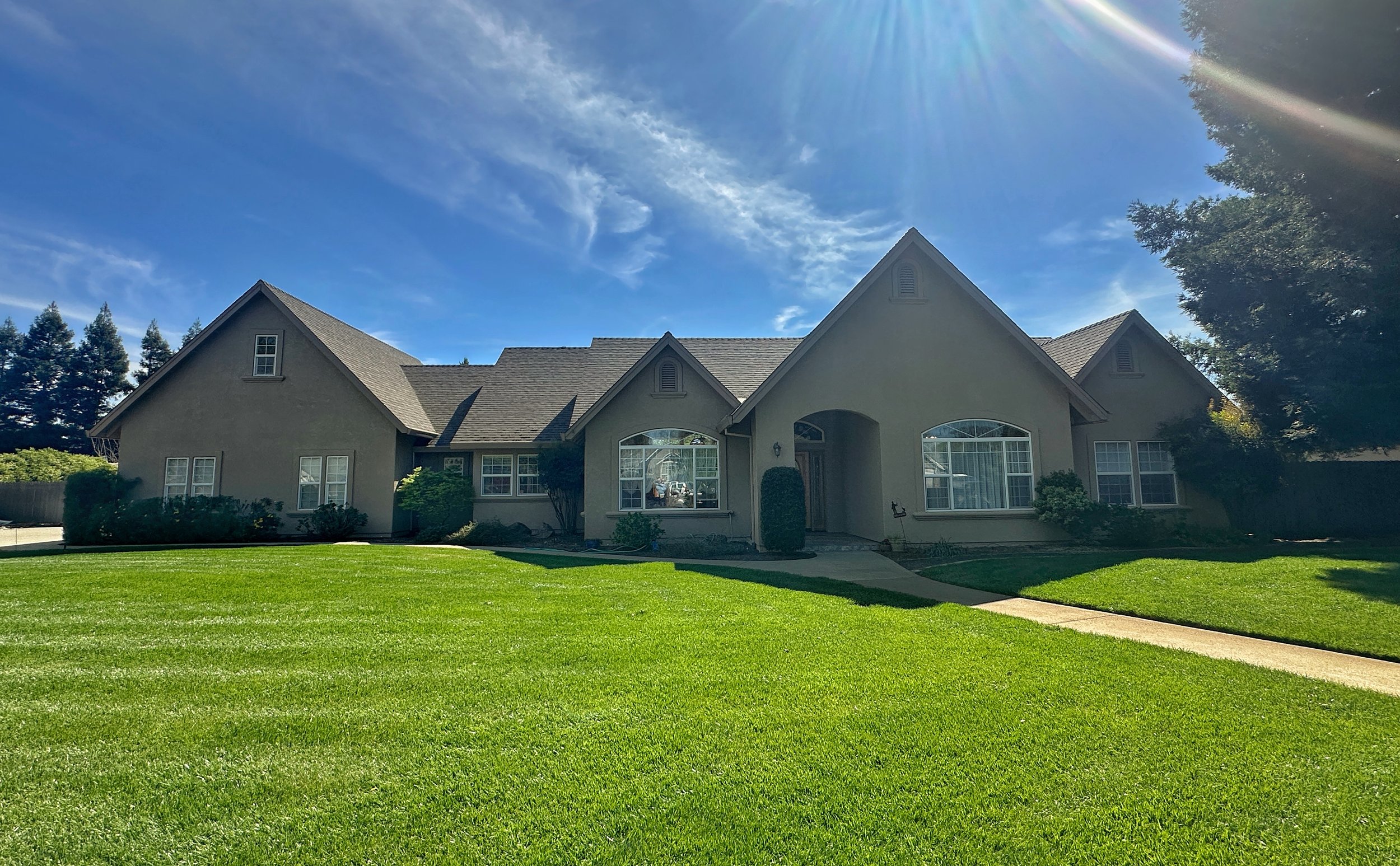 Front view of a large house with a well-maintained lawn under a clear blue sky with the sun shining.